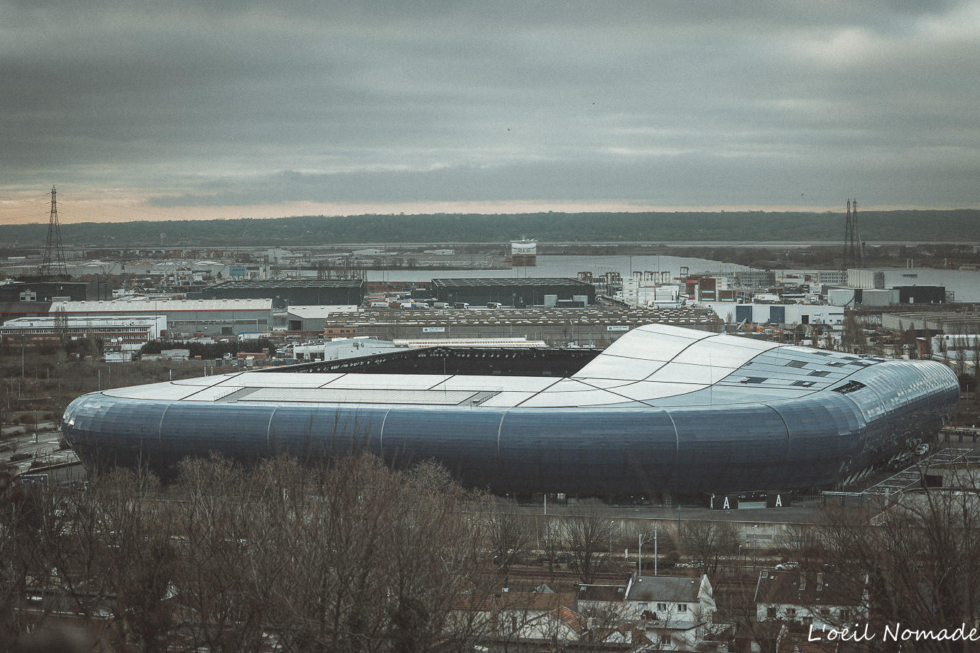 Contraste urbain : le Stade Océane vu depuis les hauteurs de l'Abbaye de Graville, ciel chargé et ambiance documentaire.