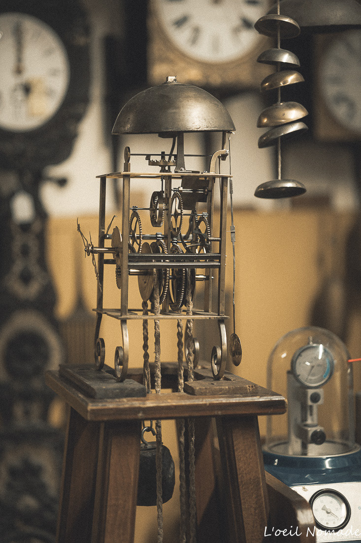 Mécanisme de pendule ancienne sur socle en bois, roues dentées et balanciers, reportage métier horloger.