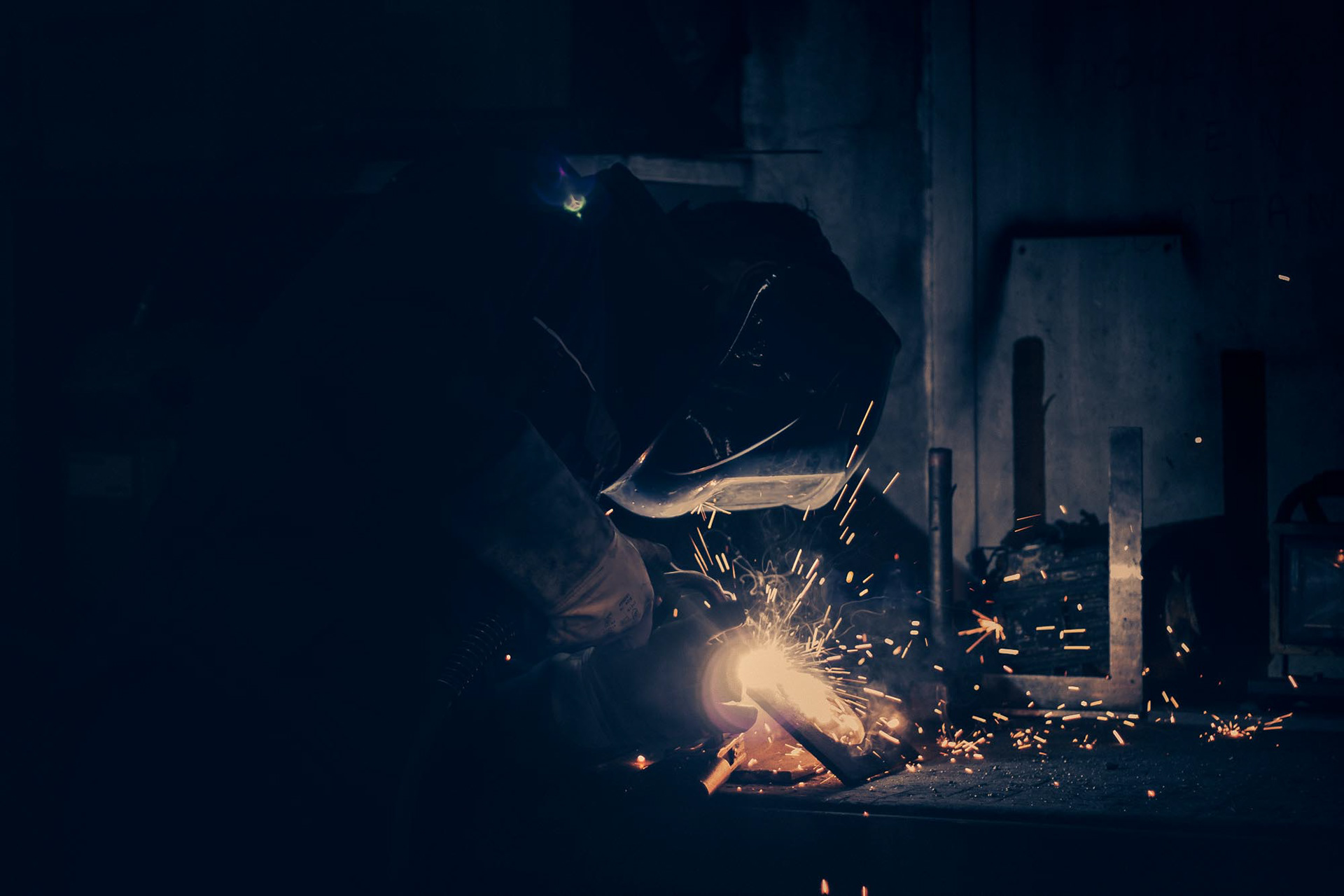 Photographie industrielle de soudure chez Jeletrans : contraste saisissant entre l'obscurité et la lumière des étincelles, valorisation du travail des métaux au Havre.