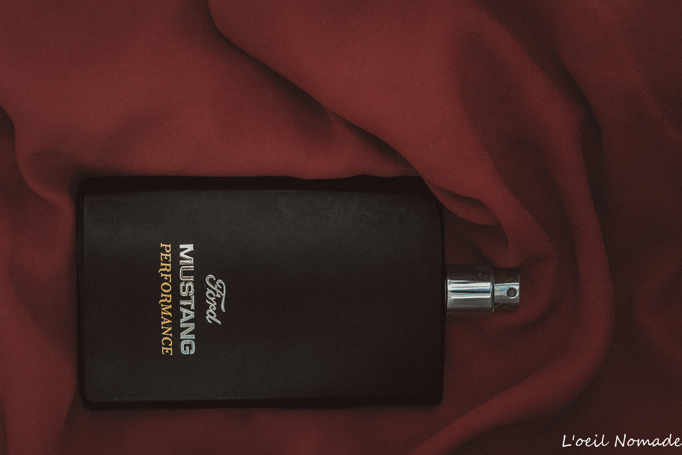 Flacon de parfum Mustang Performance sur drapé rouge profond, élégance et clair-obscur