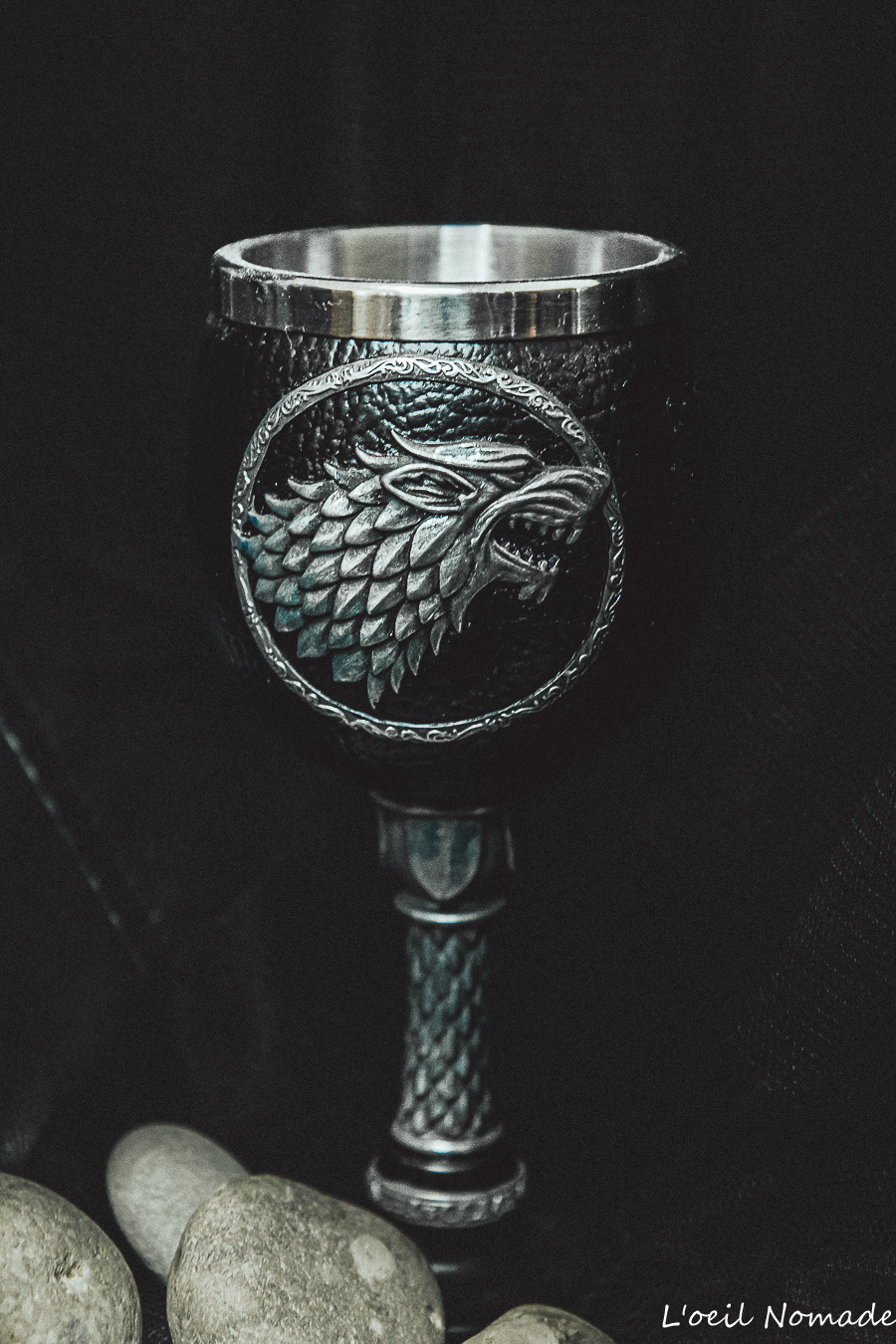 Photographie d'objet : calice orné d'un loup (Stark) sur fond noir, éclairage dramatique soulignant les détails métalliques.