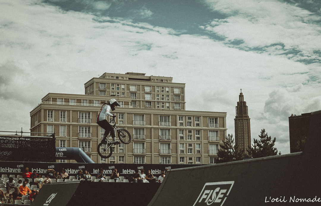 Photographie de sport au Havre : saut d'un athlète BMX avec l'église Saint-Joseph et l'architecture Perret en arrière-plan, reportage lors du Week-end de la Glisse.