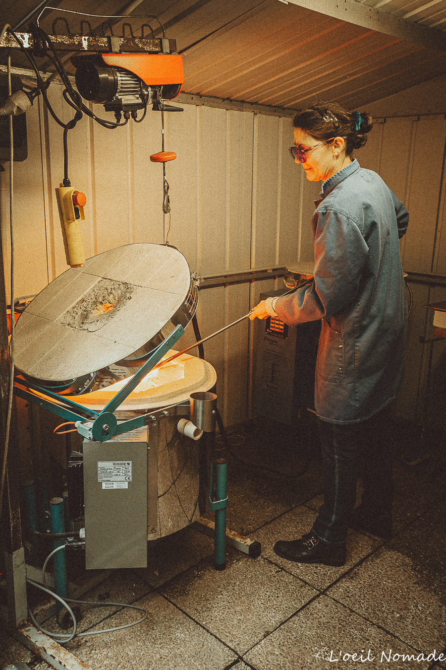 Photographie d'artisanat d'art : Chrystelle, souffleuse de verre, prélevant la matière en fusion au four, gestion des contrastes de lumière et de chaleur.