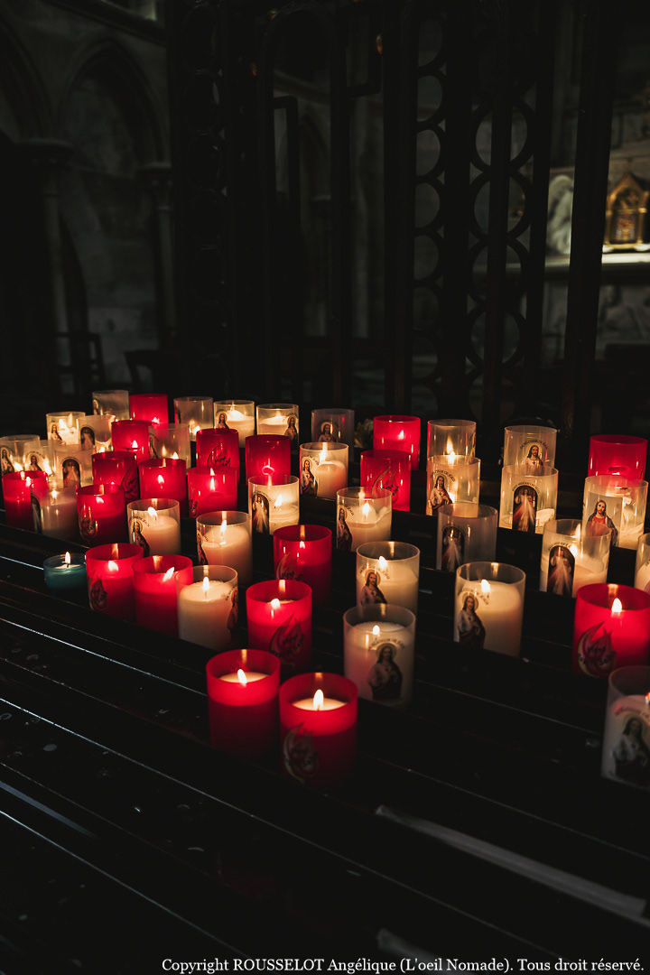Ambiance et lumière : rangées de cierges allumés dans la nef obscure de la Cathédrale de Rouen, photographie documentaire.