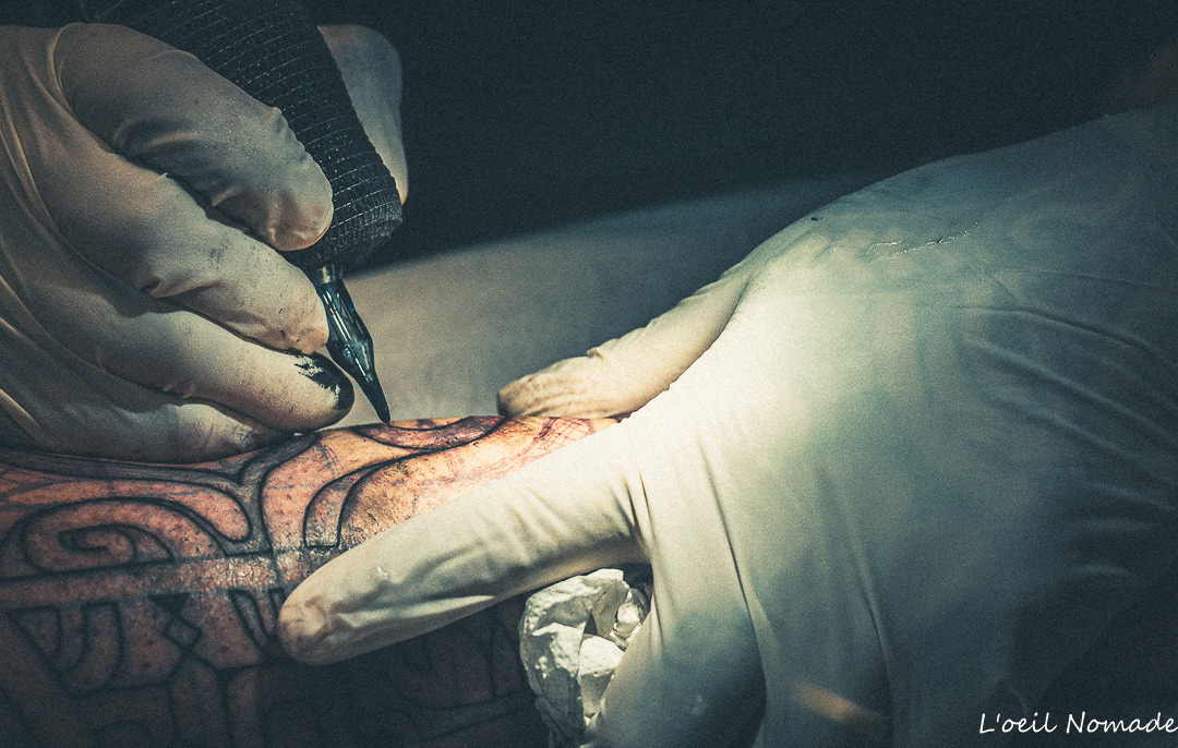 Détail macro d'un geste de tatouage précis, gants blancs et encre noire, style photographique Dark Muted avec noirs profonds.