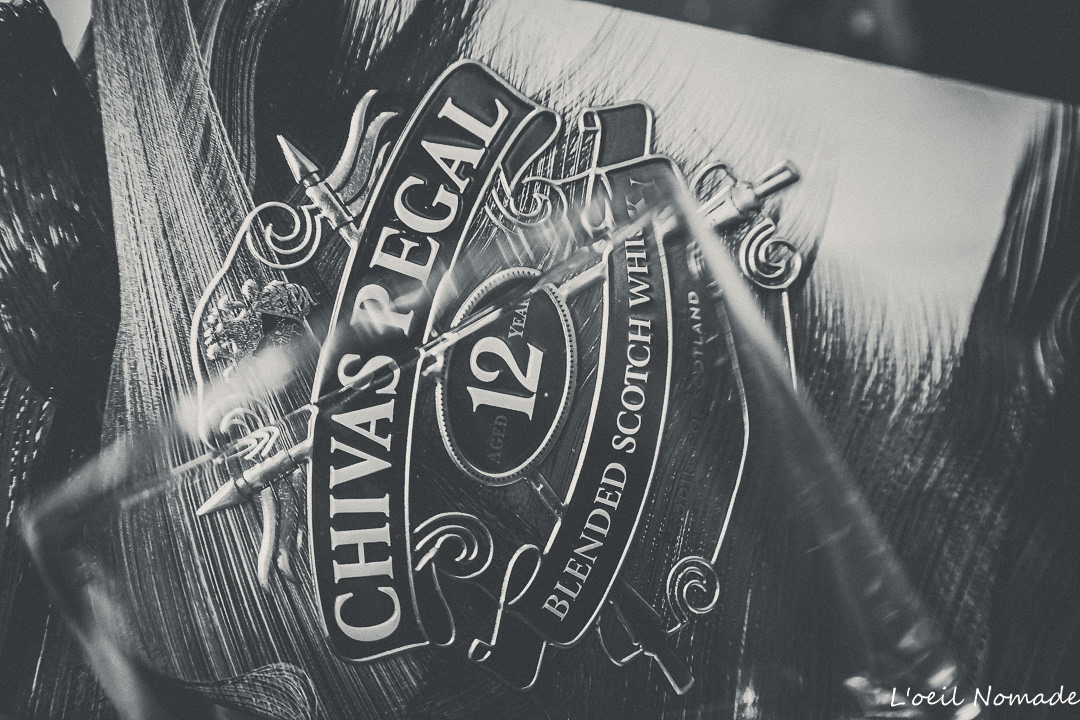 Packshot de luxe : détail de l'étiquette d'une bouteille de whisky Chivas Regal, jouant sur les reflets du verre et la profondeur de champ.