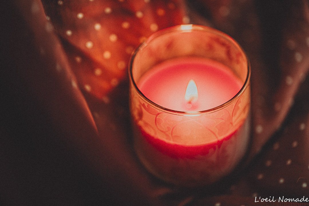 Photographie d'ambiance packshot : bougie allumée sur fond de tissu à pois, travail sur la lumière chaude et la douceur des matières pour marque de décoration.