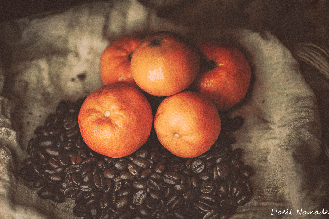 Nature morte : gros plan sur des grains de café torréfiés et des oranges, travaillant la complémentarité des couleurs et des textures.