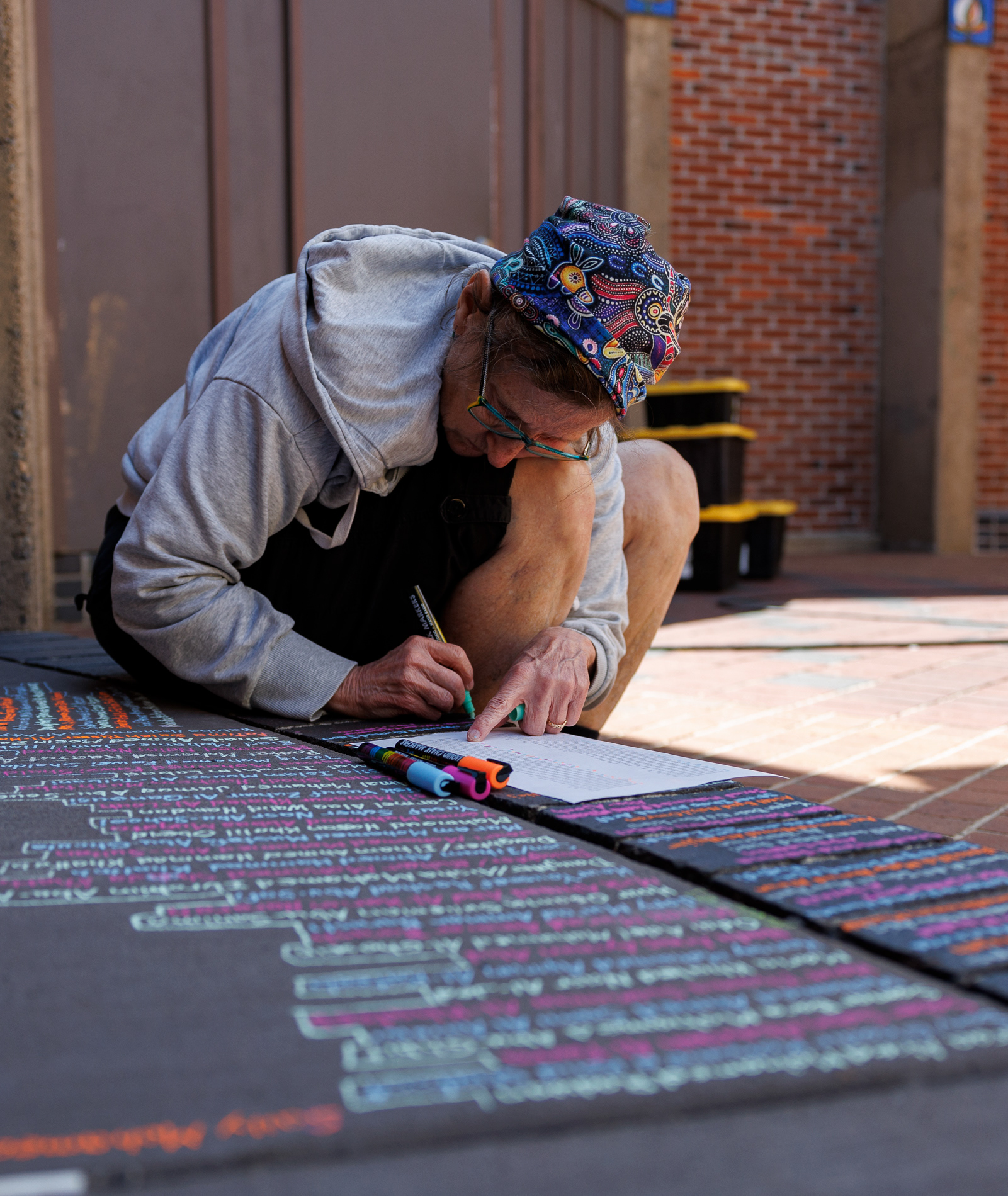 A person writes names from a 111-page list of people killed in Gaza during a "Children of Gaza" community art event at Kesey Square on July 4, 2025. | Shot for Emerald Media Group | 1/500 f/2.8 ISO100