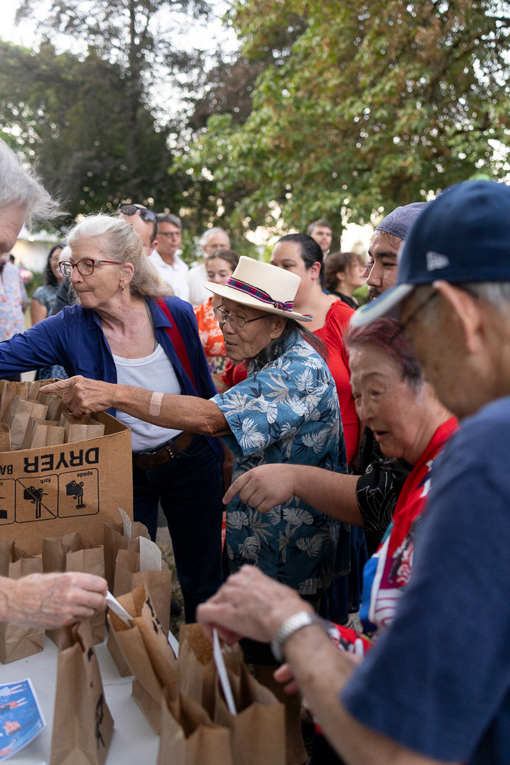 People line up to grab paper lanterns, which were released as part of a lantern ceremony at the Hiroshima-Nagasaki commemoration event at Alton-Baker Park on August 6, 2024. People gathered to commemorate the 1945 bombings with speakers, performances and more, concluding the event with a lantern ceremony. | Shot for Emerald Media Group | 1/250 f/2.8 ISO3200