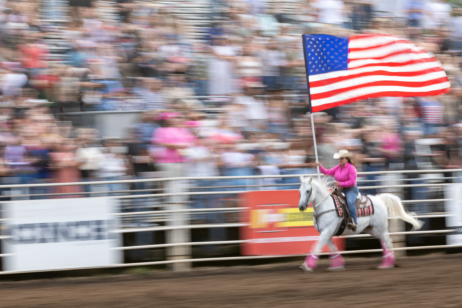 A rider carries the American flag around the arena at the Eugene Pro Rodeo on July 3, 2025. The night's theme was "Tough Enough To Wear Pink," a campaign promoting breast cancer awareness. | Shot for Emerald Media Group | 1/15 f/8 ISO100