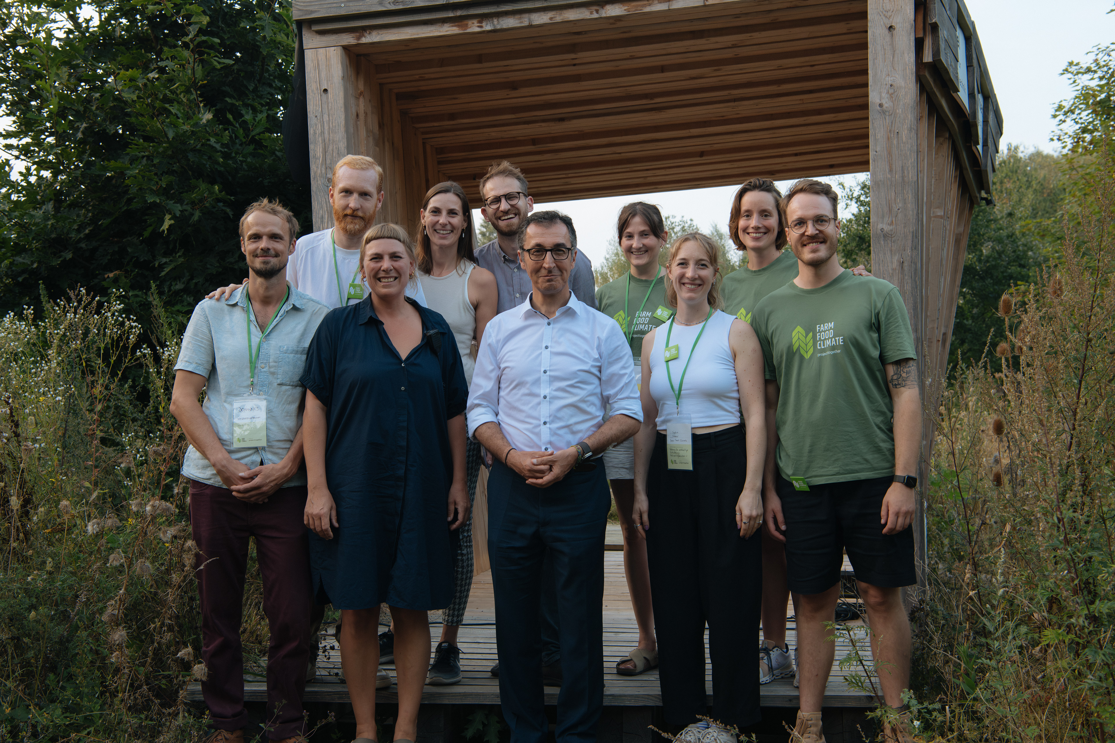 Gruppenporträt mit Cem Özdimir und Teilnehmenden des Farm Food Climate Festivals vor einem Holzgebäude.