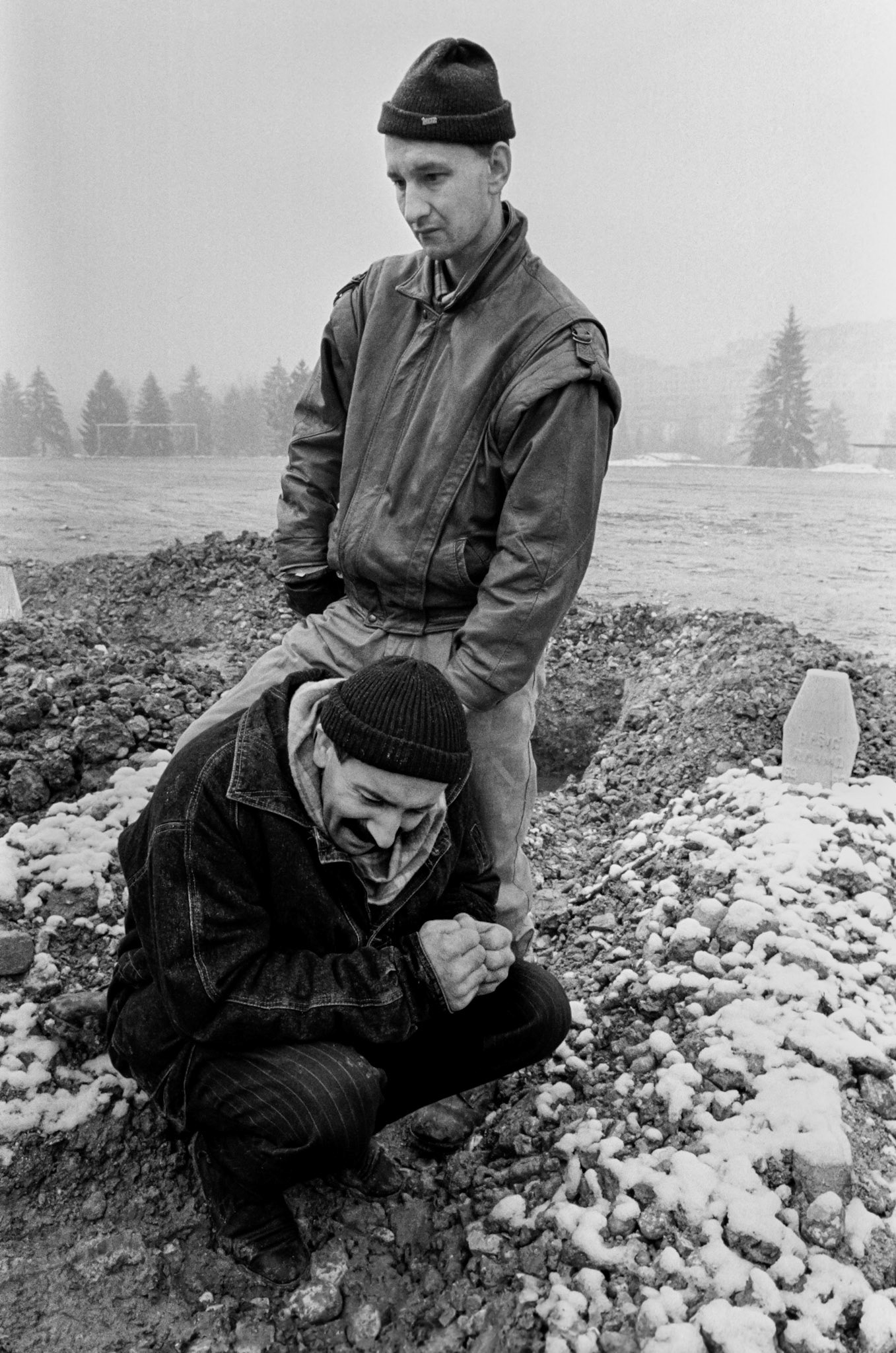Two Bosnian men grieve at a friend's grave in a makeshift cemetery in a soccer field in Sarajevo on December 10, 1993.