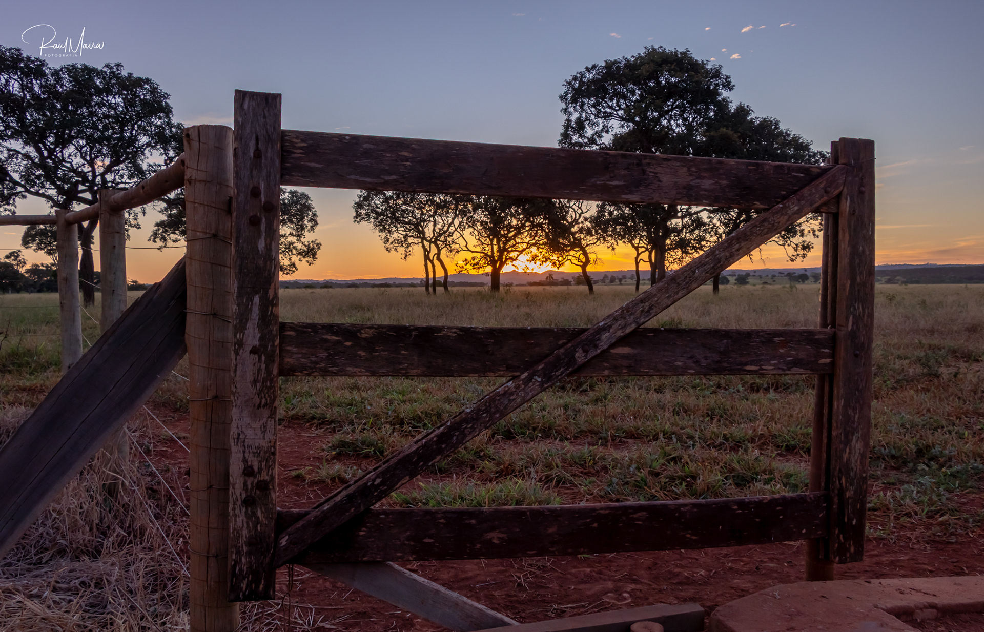 Porteira com o pôr do sol no campo.