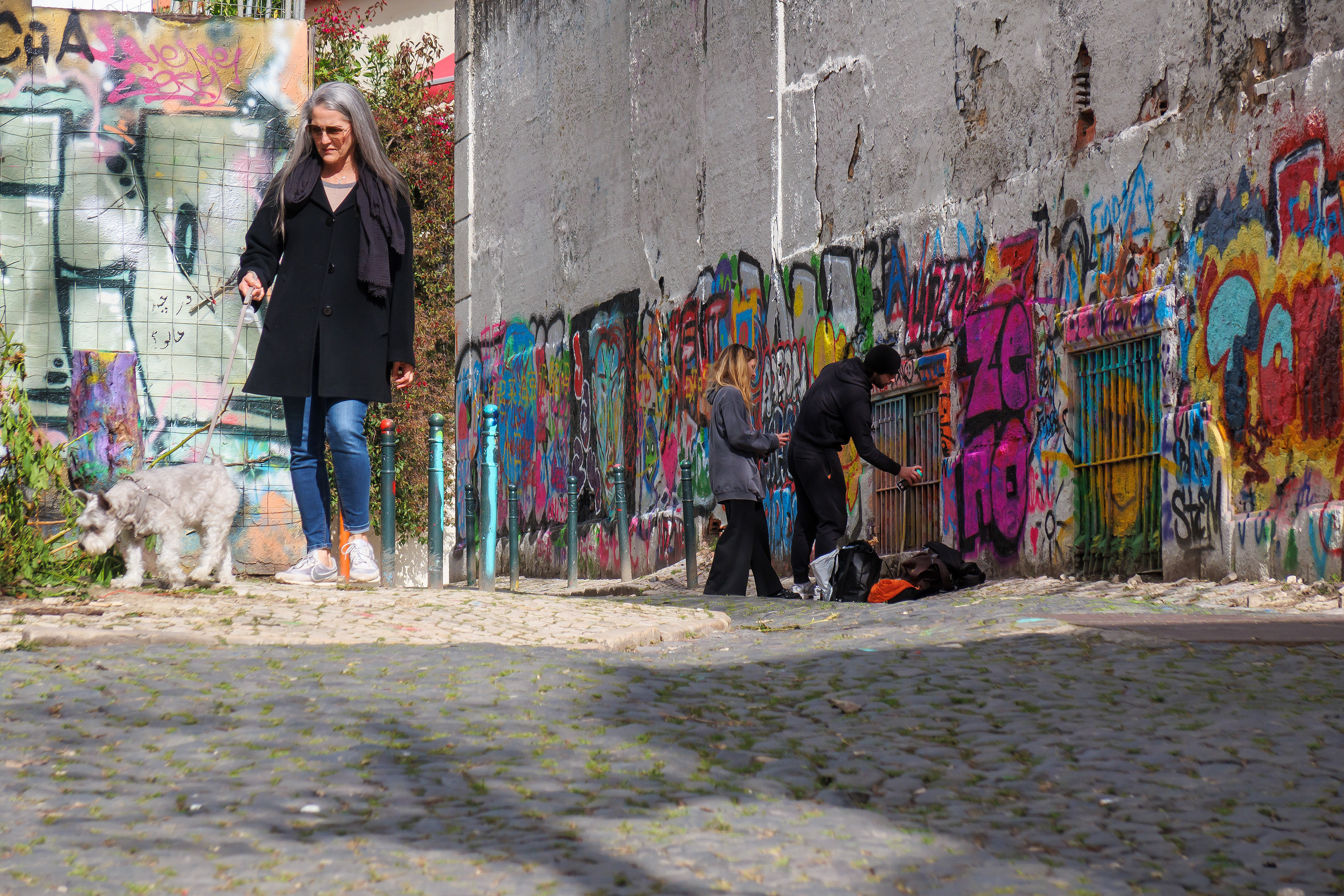 Dog walker ignores graffiti artists near a tourist hot spot in Lisbon