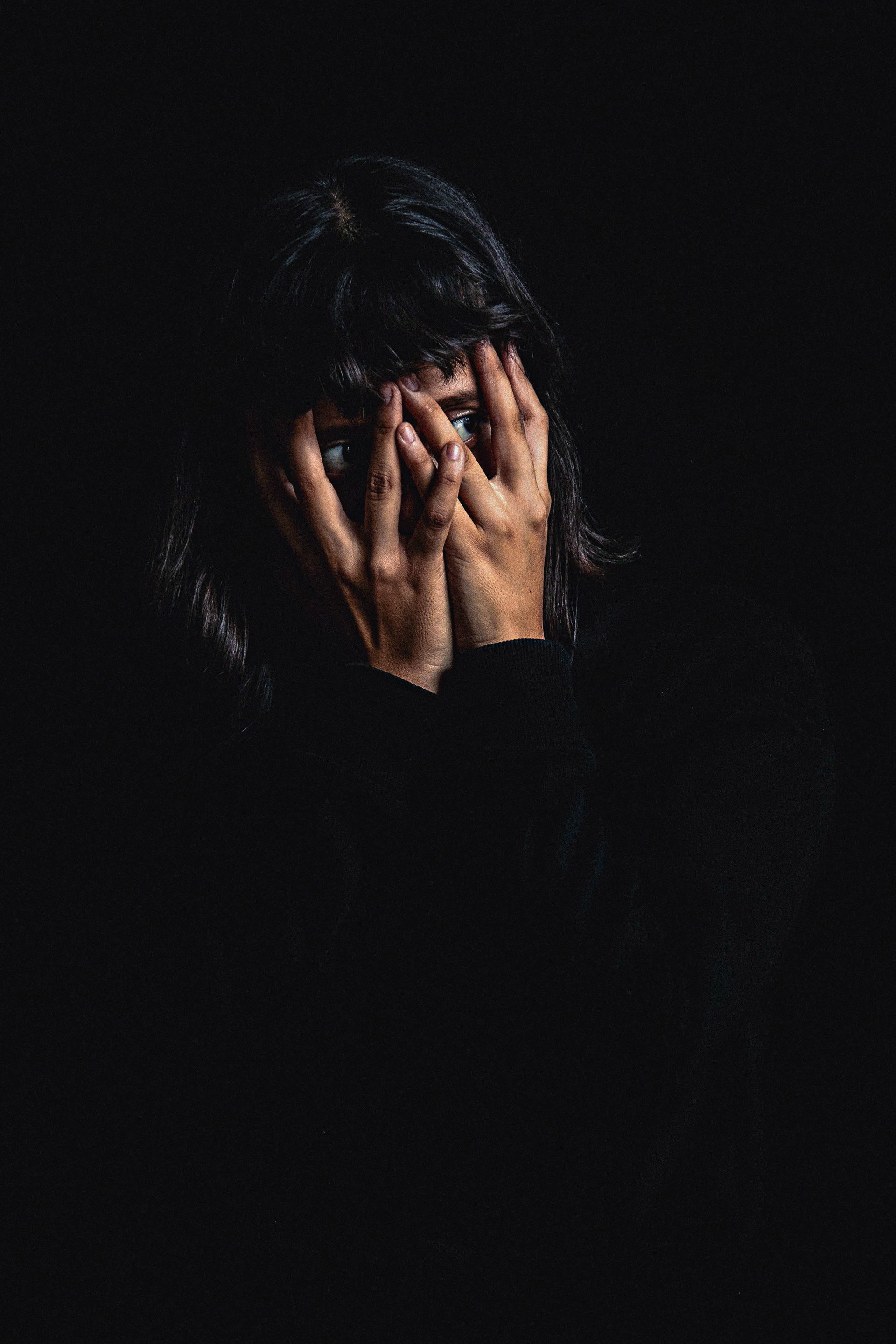 ditorial portrait photography of a woman partially covering her face with her hands, using dramatic lighting, negative space and fine art composition to explore identity and perception.