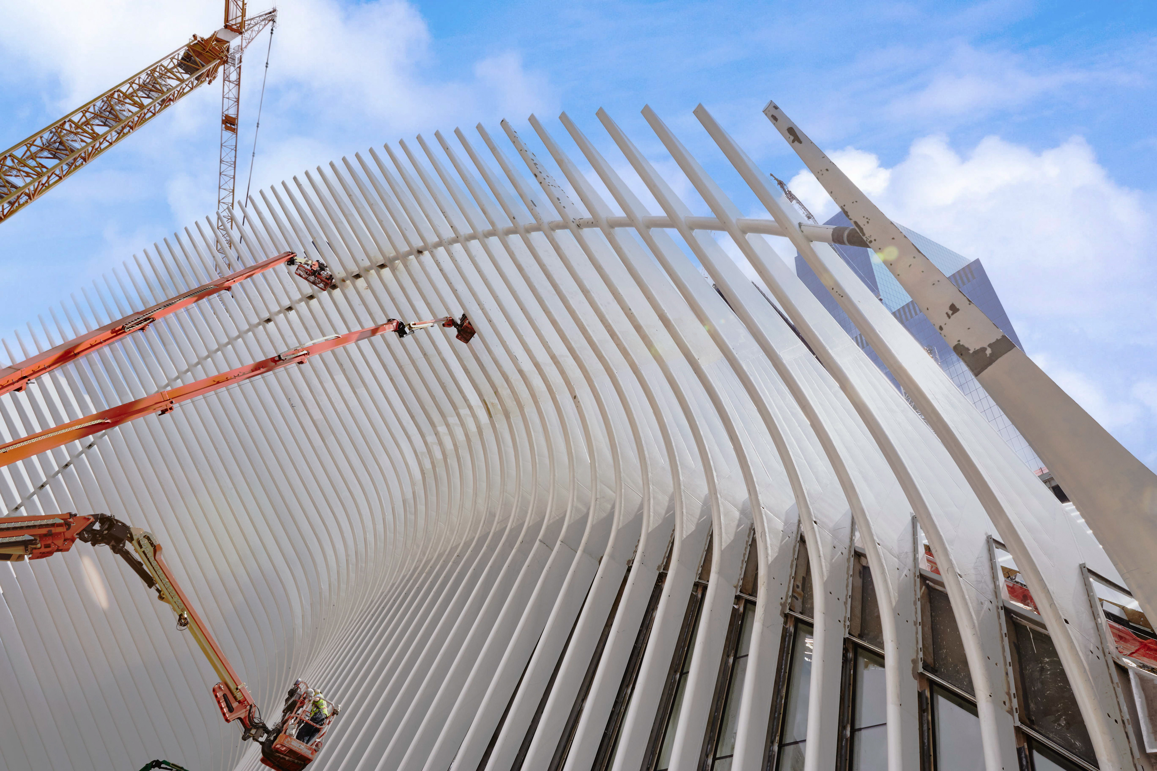 World Trade Center Oculus under construction in Lower Manhattan, photographed from outside with workers, lifts, cranes, and the white ribbed structure.