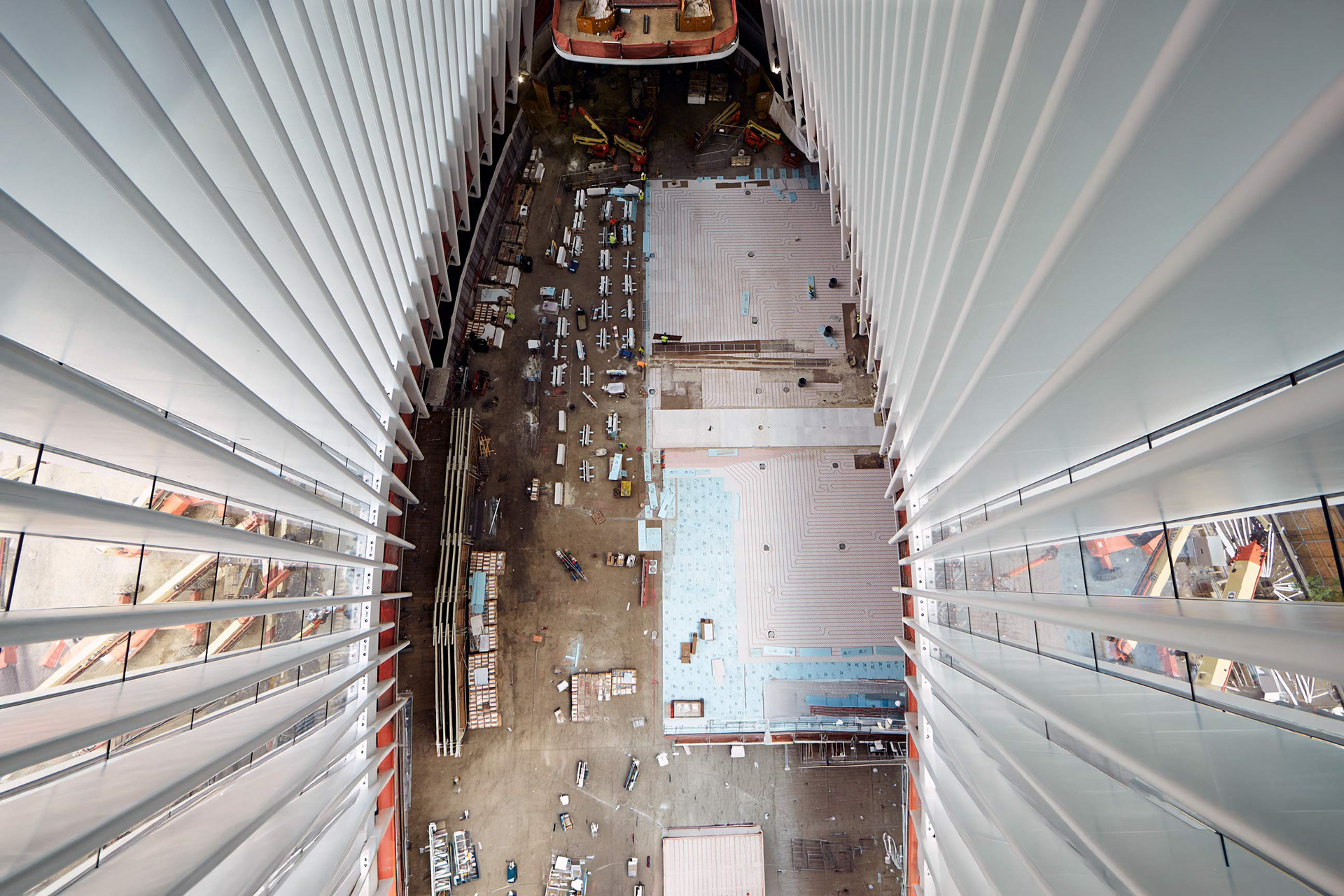 World Trade Center Oculus main floor photographed from above during construction, showing workers, materials, and the unfinished interior from a restricted rafter perspective.