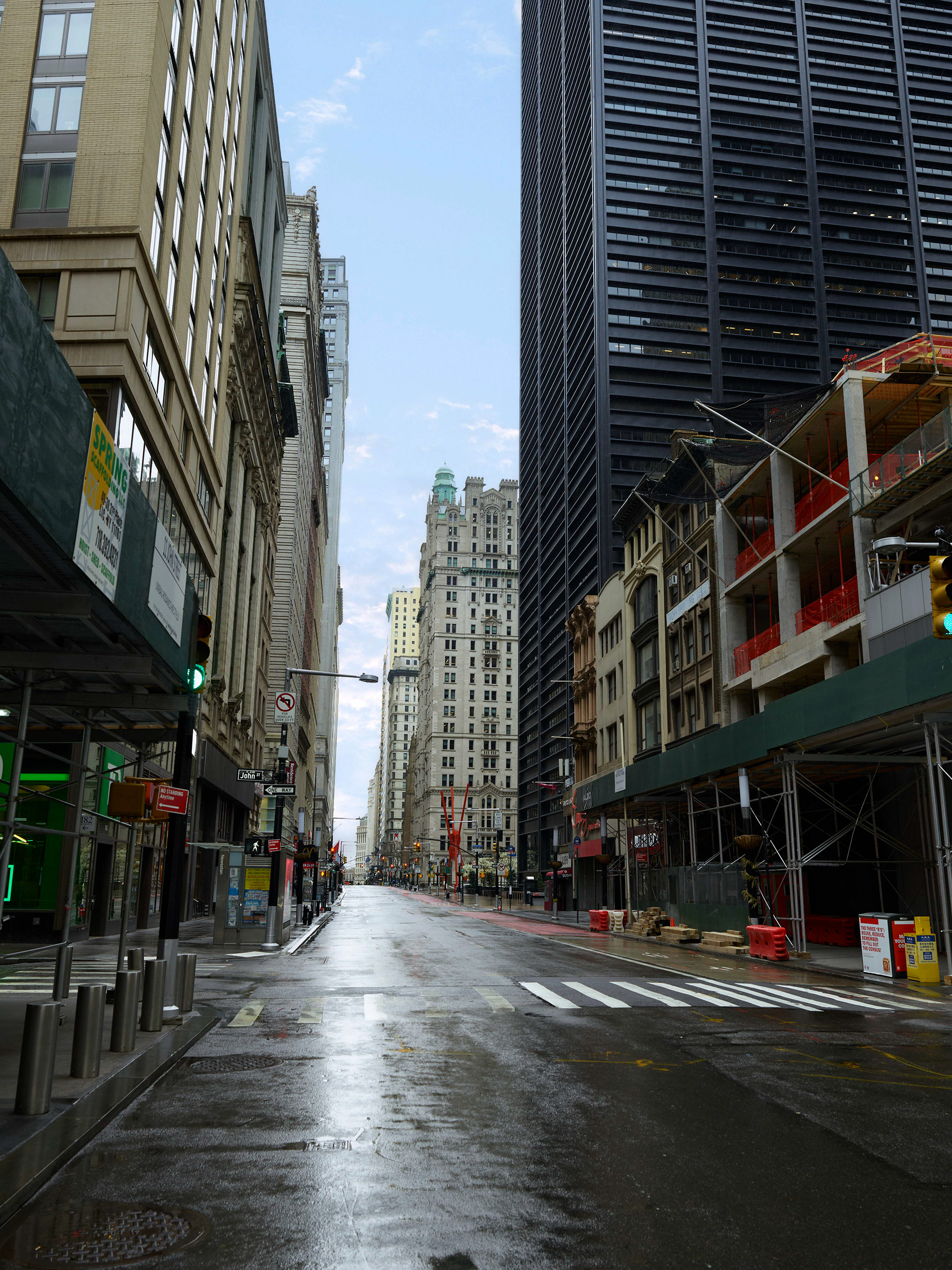 Quiet downtown New York City street during Covid, photographed in Lower Manhattan with wet pavement and empty traffic lanes.