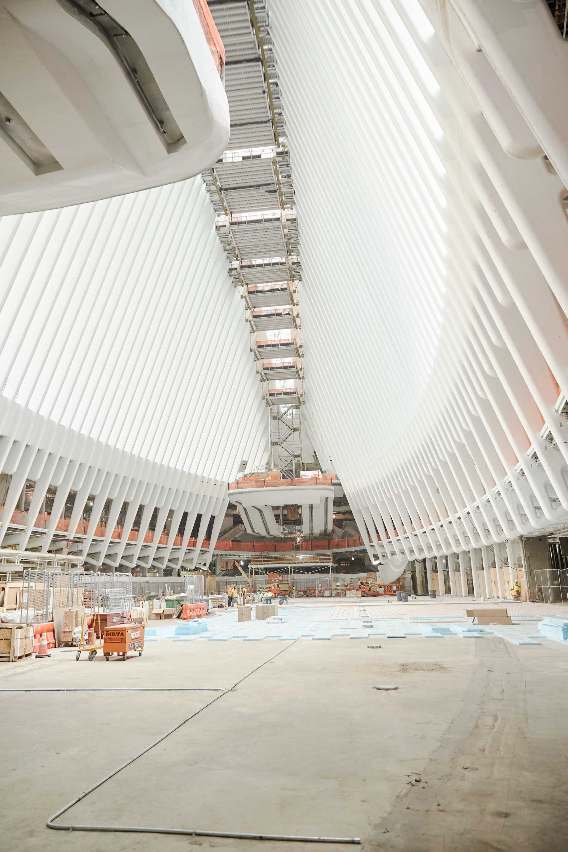 World Trade Center Oculus under construction from the main floor, showing the white ribbed architecture, scaffolding, lifts, and unfinished interior.