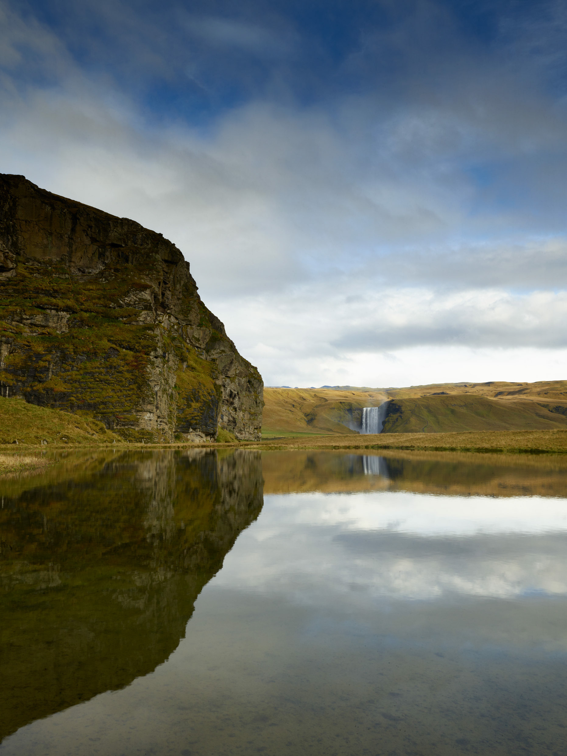 Wide view of Iceland waterfall flowing into water surrounded by cliffs and open sky