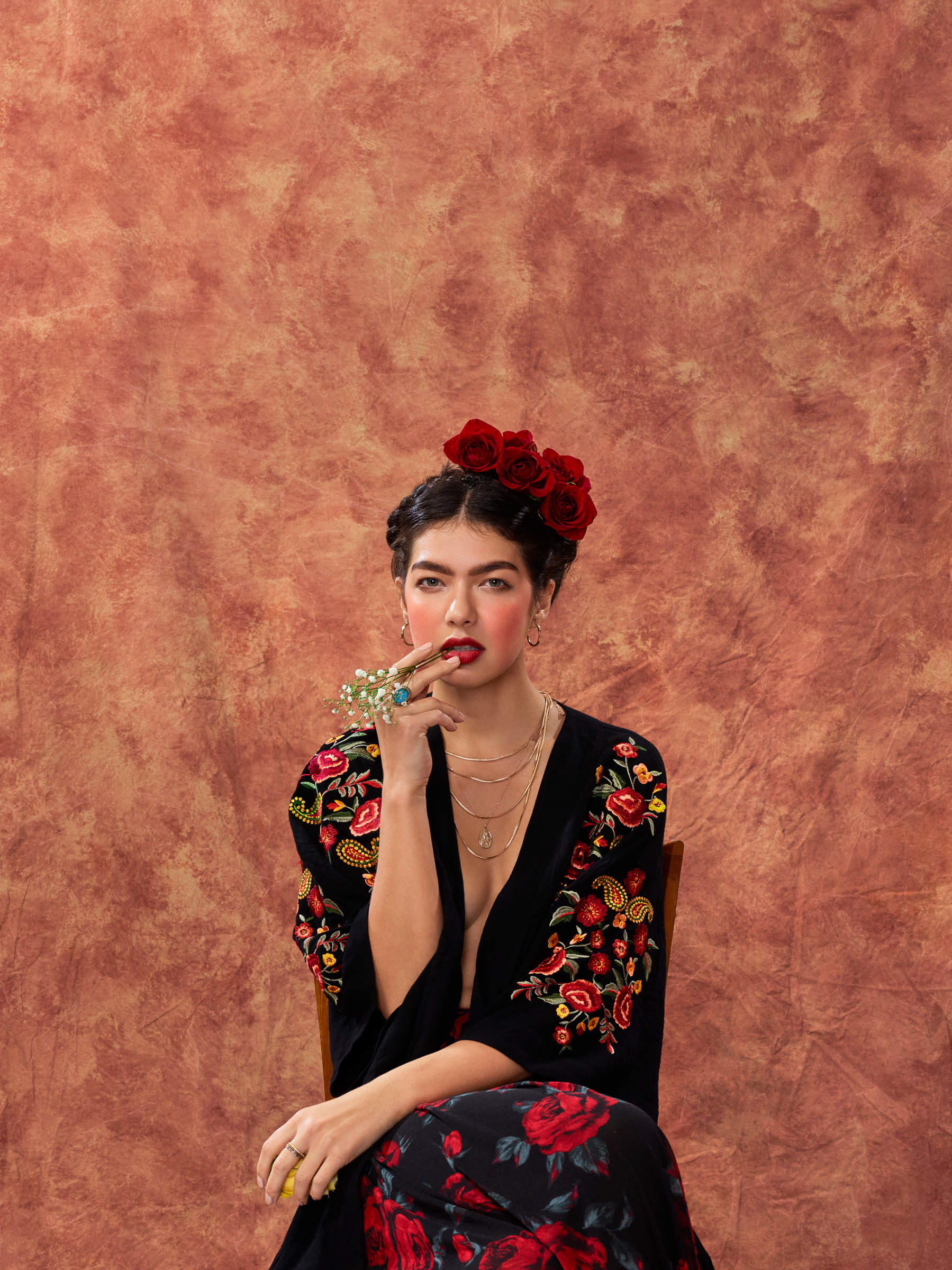 Frida inspired portrait of woman seated with flower stem in mouth looking at camera