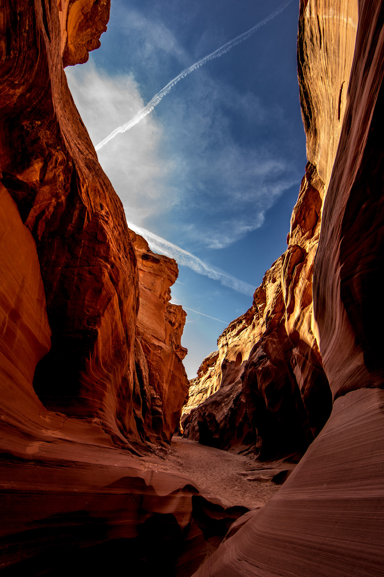 Antelope Canyon interior looking up toward blue sky and clouds framed by red sandstone