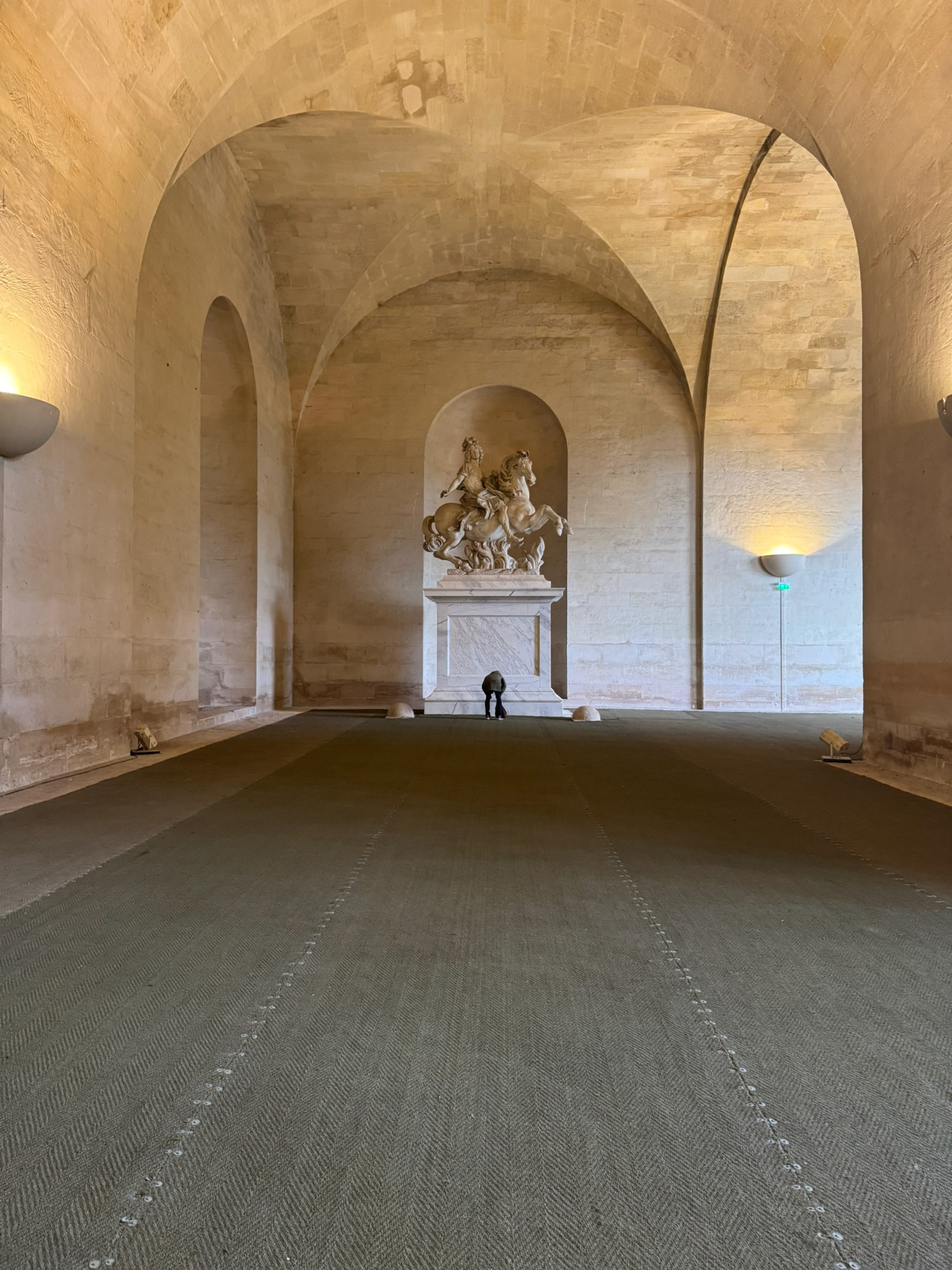 Large interior hall under Versailles with equestrian statue and person reading plaque