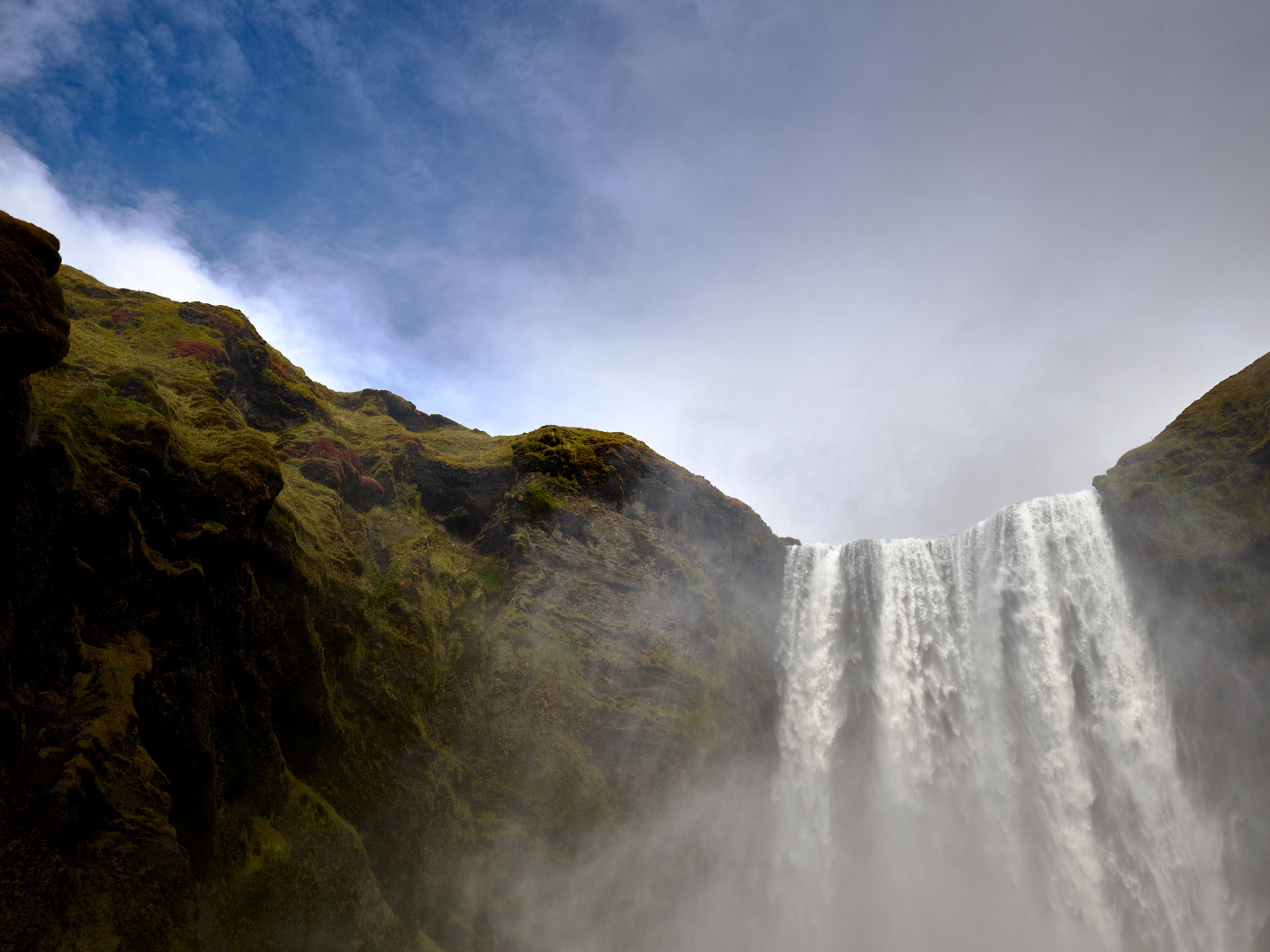 Waterfall near Vik Iceland with cascading water, mist, and blue sky