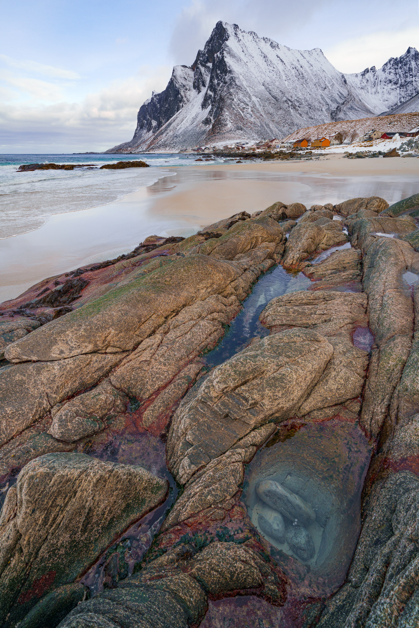 Beautiful rocks at the sea side and a small village in the distance. Red algae coloring the rocks.