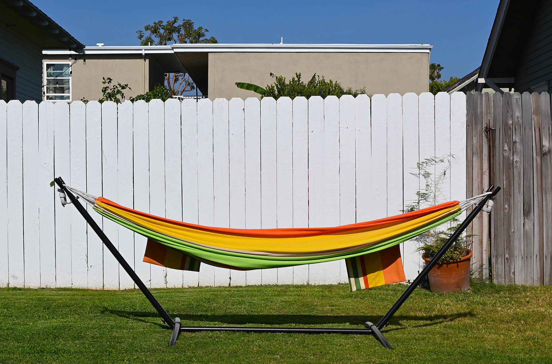 Hammock on a lawn in front of a white wood fence.