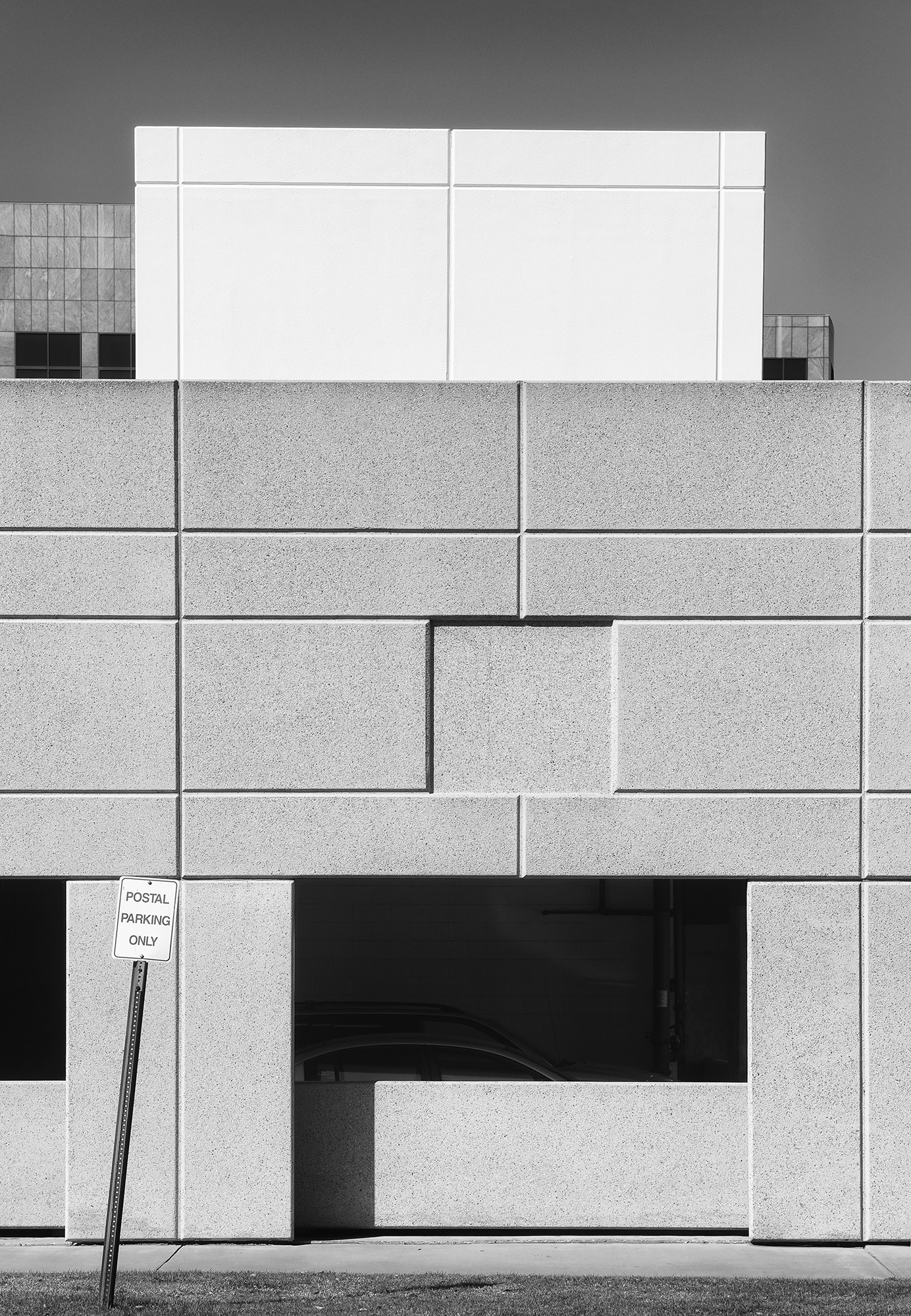 Crooked Postal Parking Only sign in front of a concrete parking structure, black and white photograph