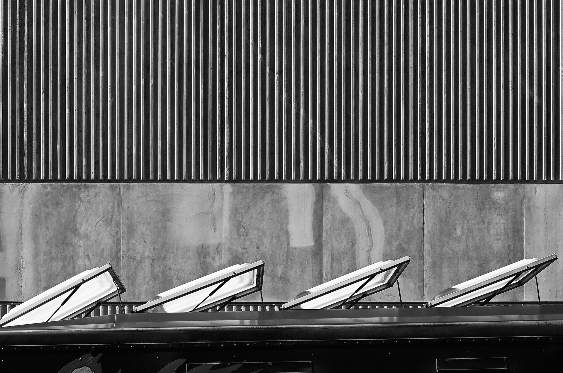The Top of a Food Trucks Roof Vents against a stark concrete building, black and white photograph