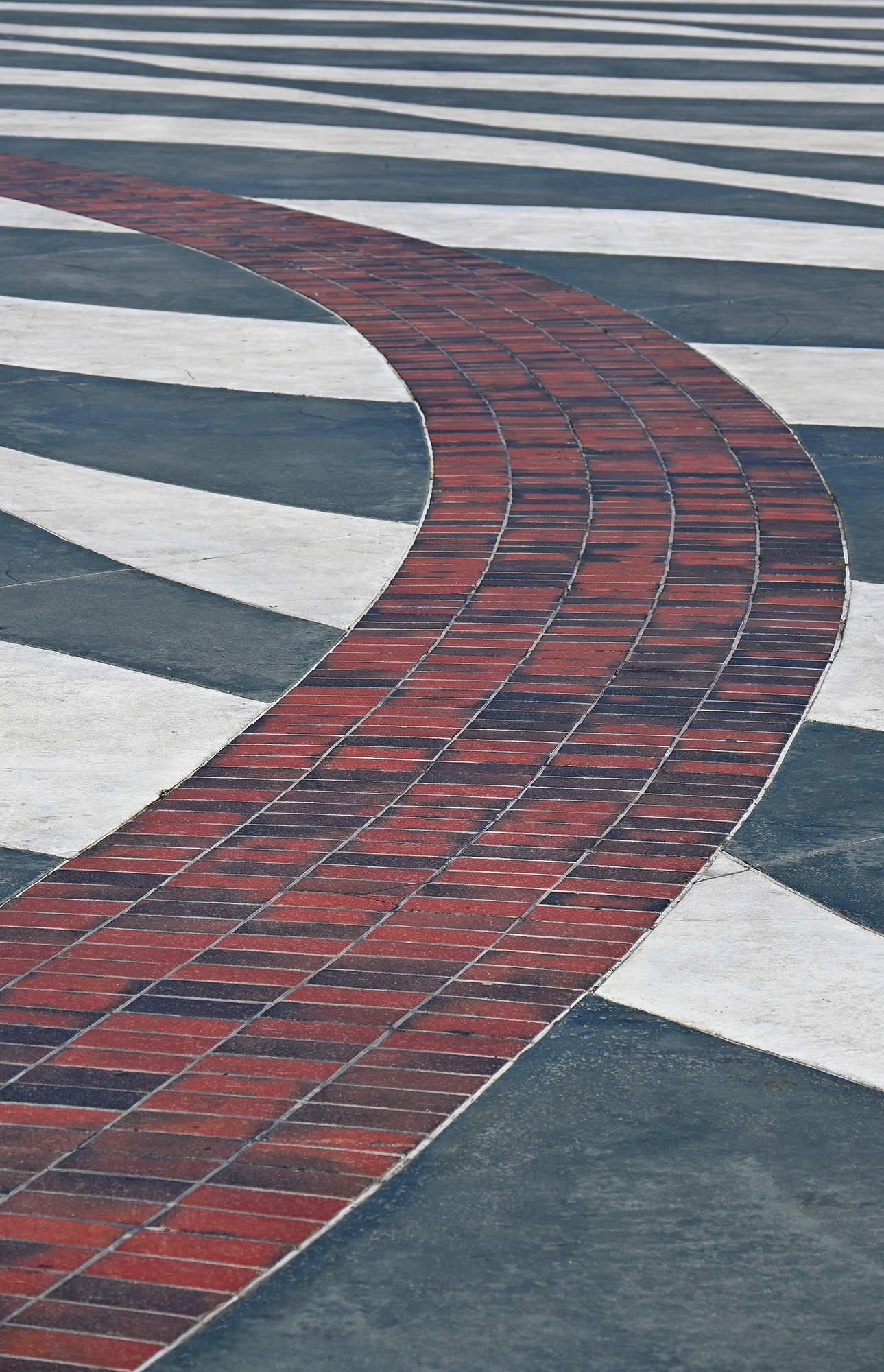 Curved Red Brick Road apt in gray and white concrete plaza.