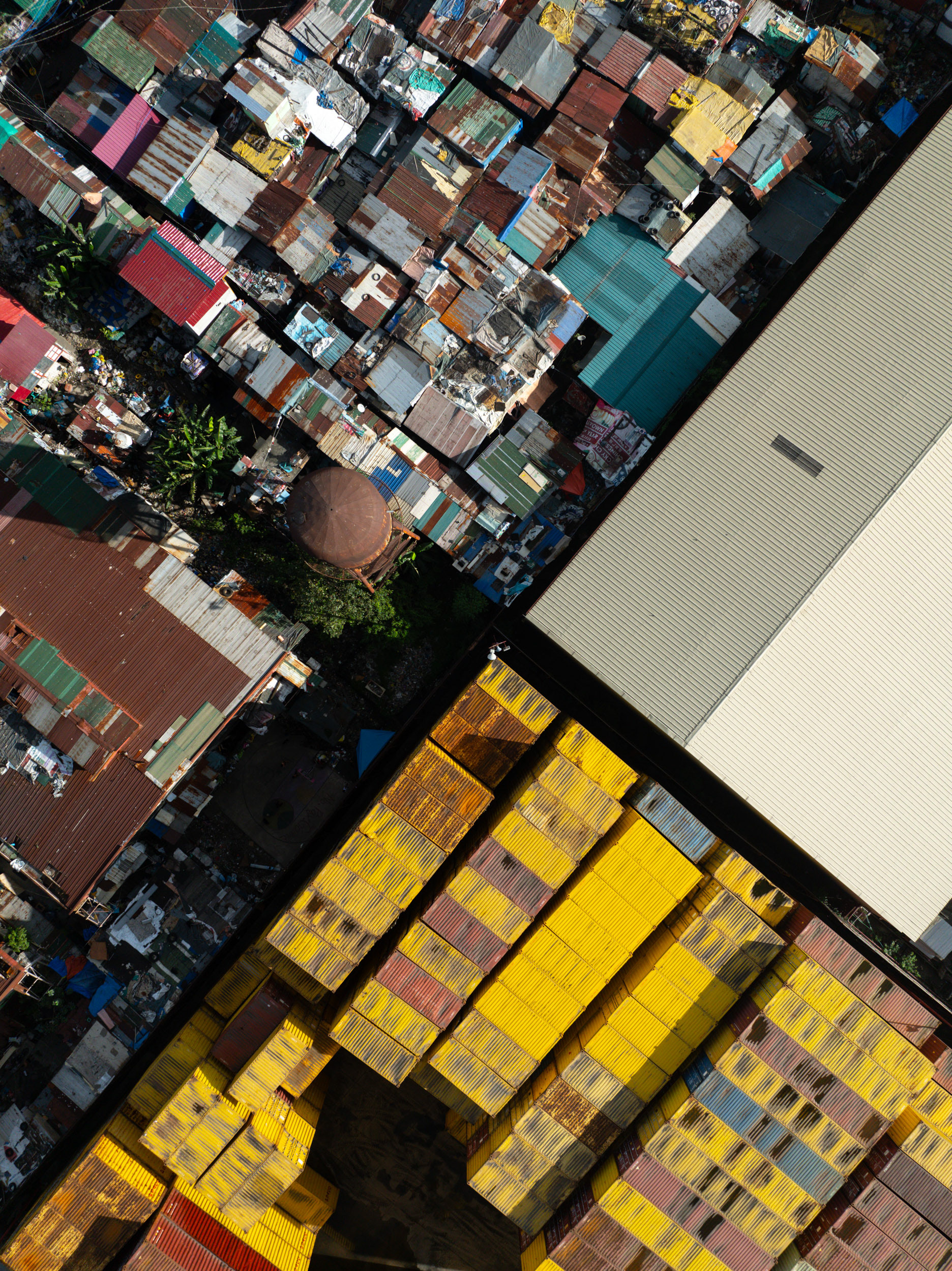 A dense cluster of homes surrounding bright yellow cargo containers at the Port of Manila.
