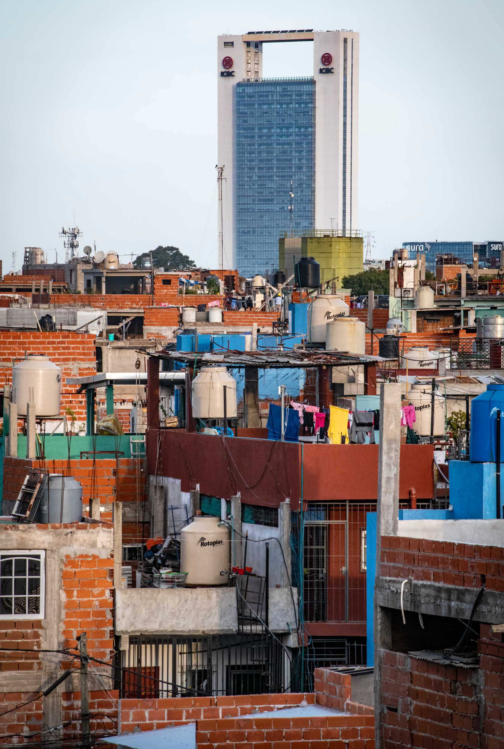 Orange brick houses in a slum with a large skyscraper bank on the horizon.