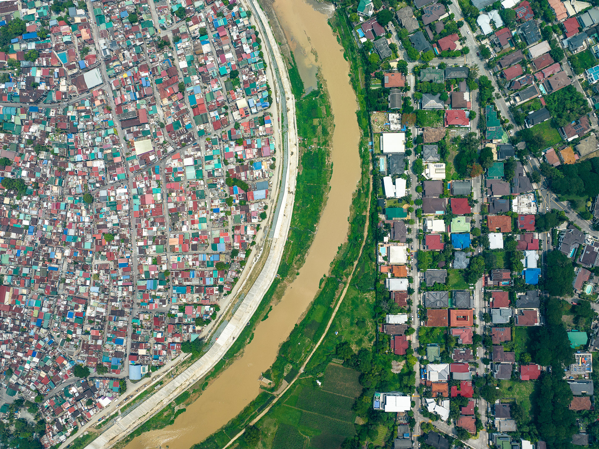 Aerial view of Pasig River dividing the informal settlement of Malanday from the middle-class neighborhood of Loyola Heights in eastern Manila, showcasing spatial inequality.
