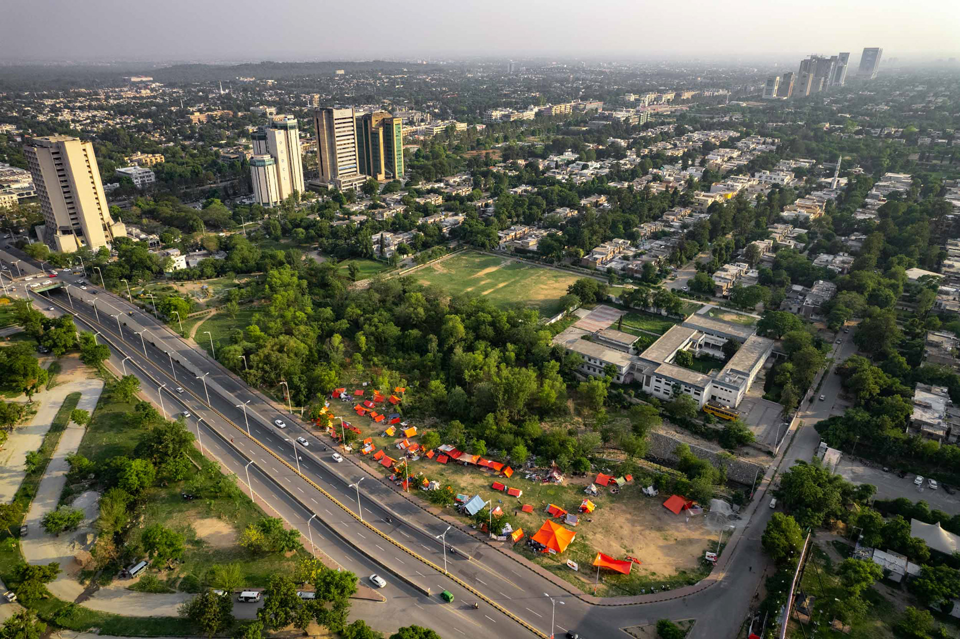 A drone view of red tents in a park in a capital city.
