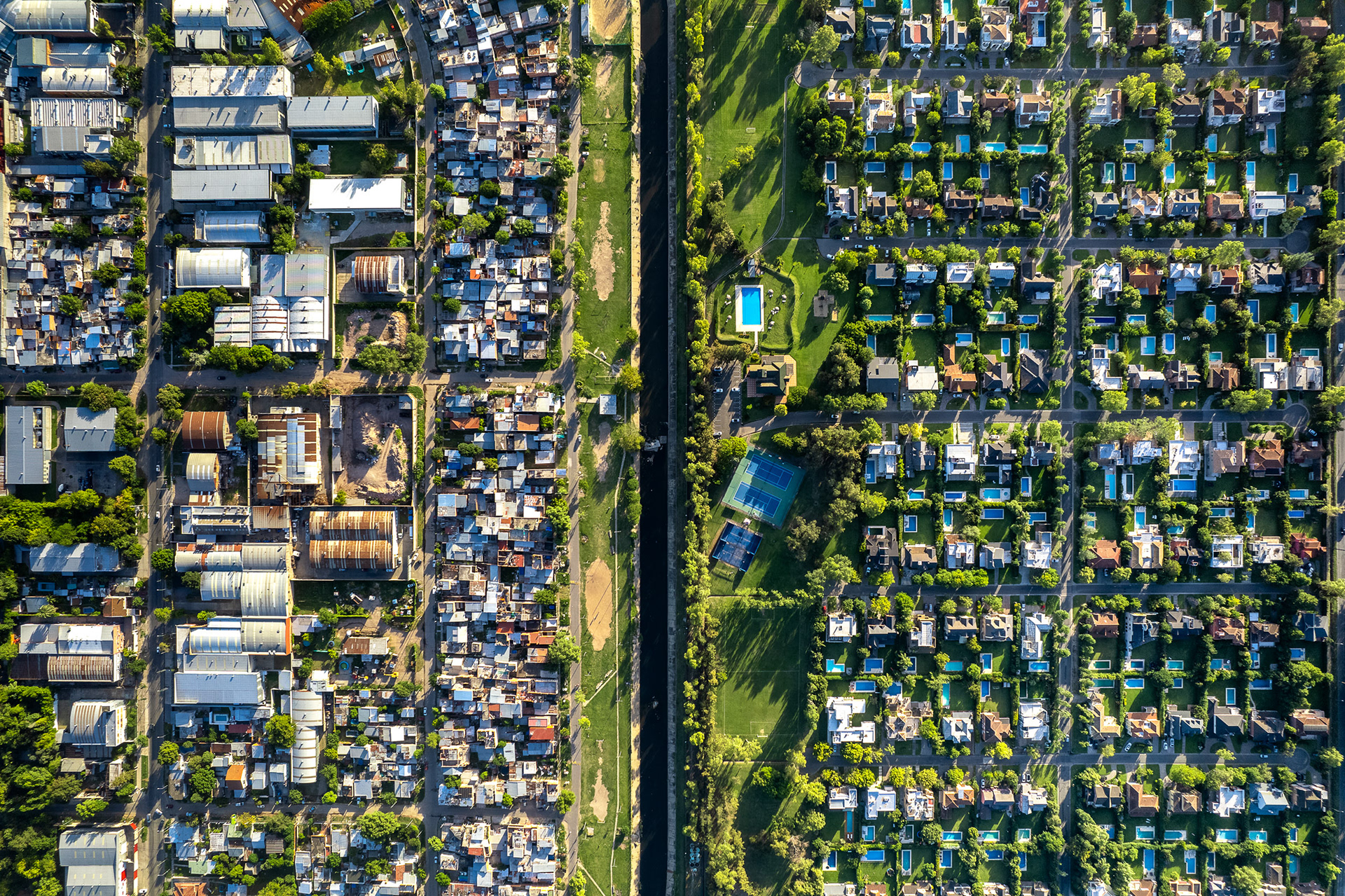 A drone photo of a slum next to a nice neighborhood with swimming pools.