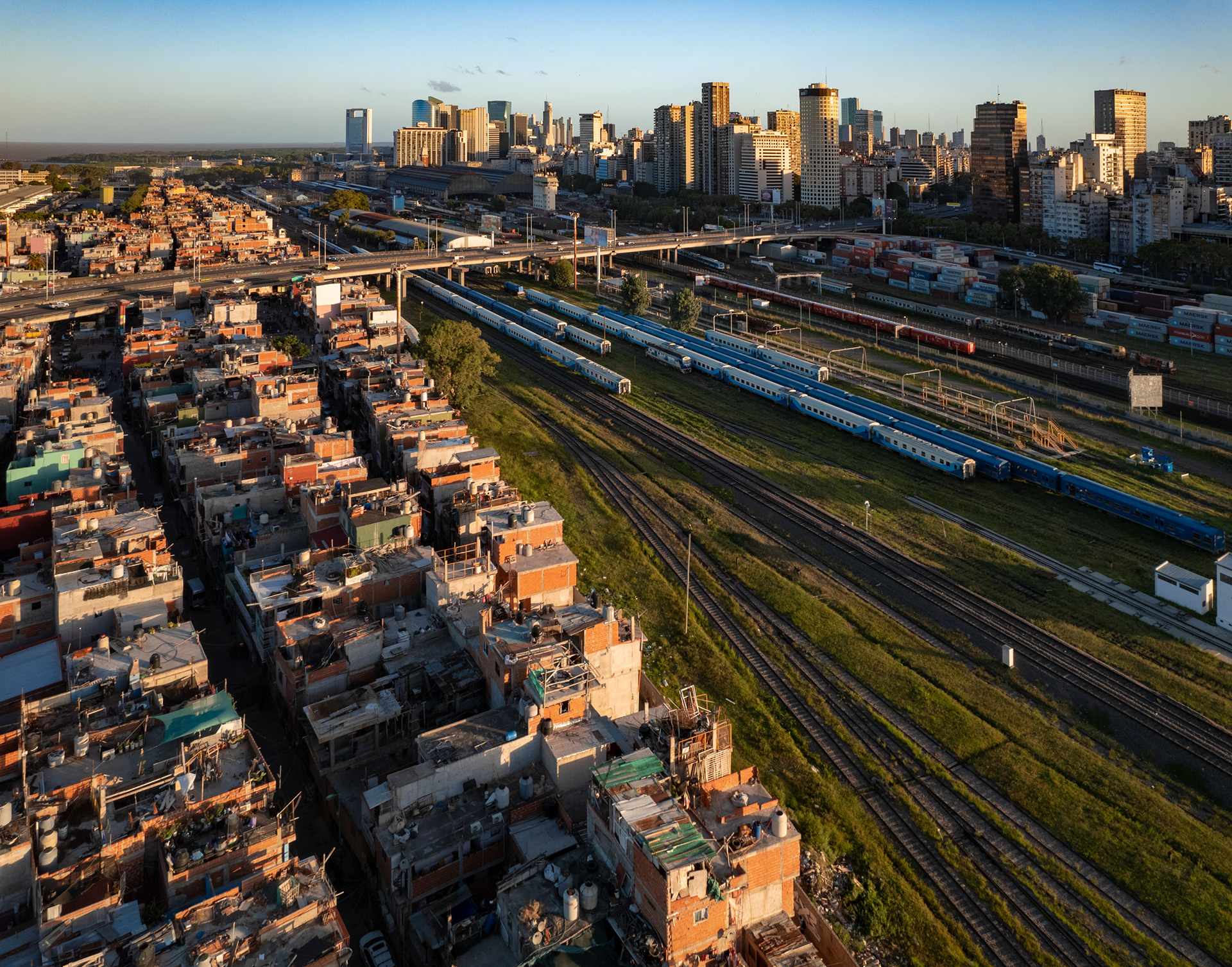 A drone photo of a train yard, a slum, and a downtown district.