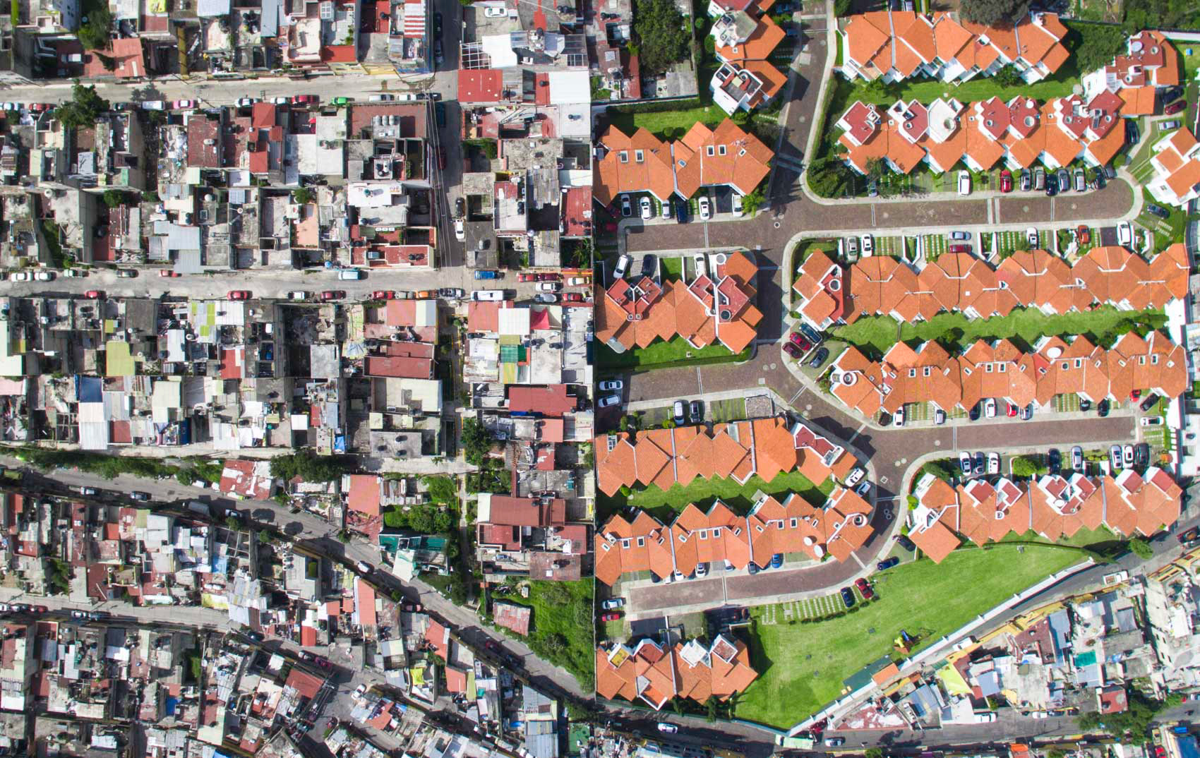 orange roof houses with green grass next to gray slums in mexico city