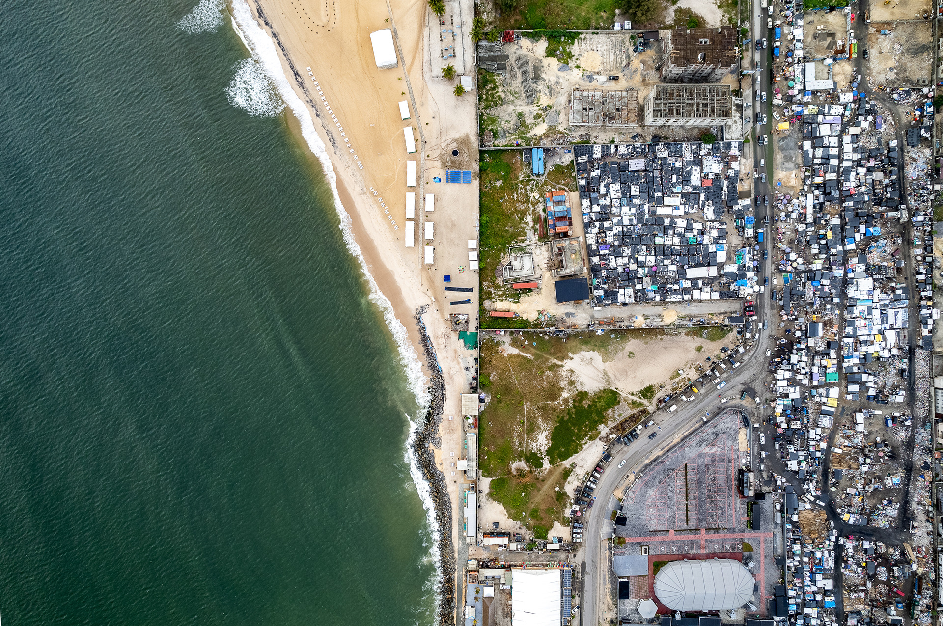 A drone view of a fence bisecting a beach club from a densely packed slum.