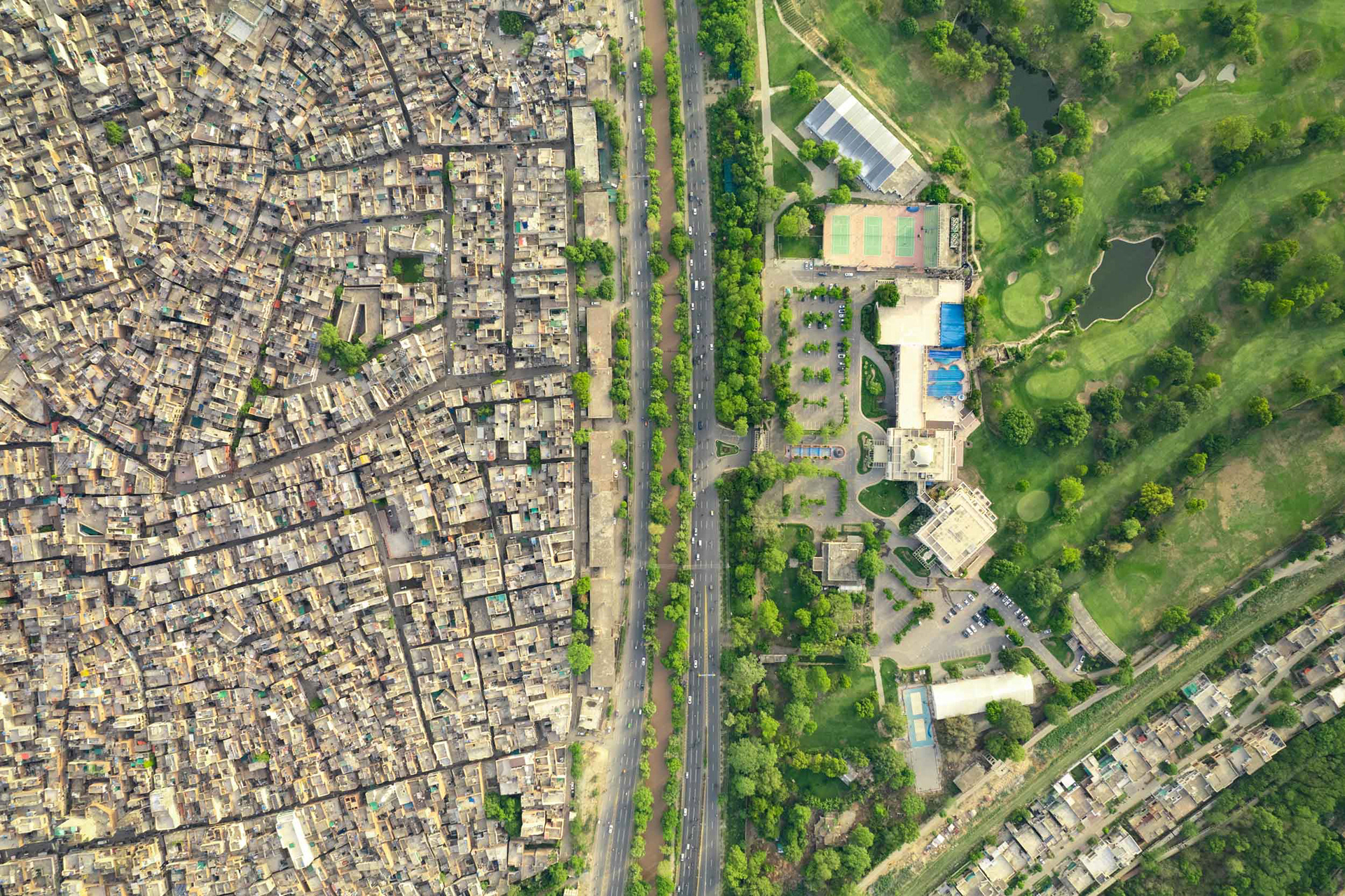 A drone view of a golf course next to a dense slum.