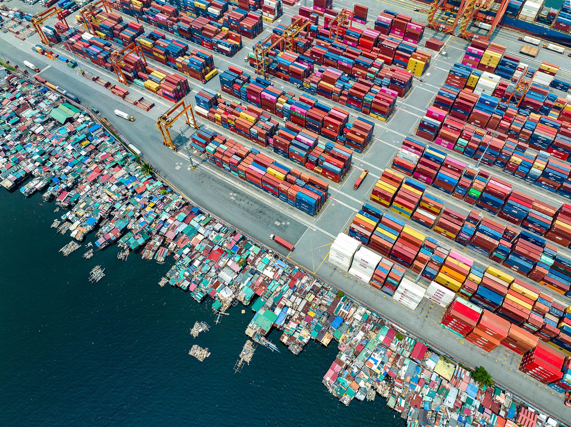 Informal floating homes beside Manila’s busy container terminal, revealing stark living condition contrast.