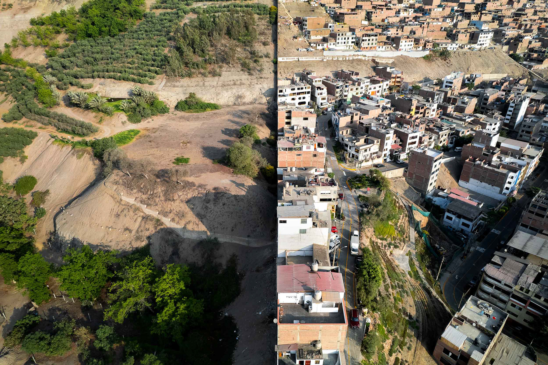 a wall separates a garden from a poor community in Lima, Peru.