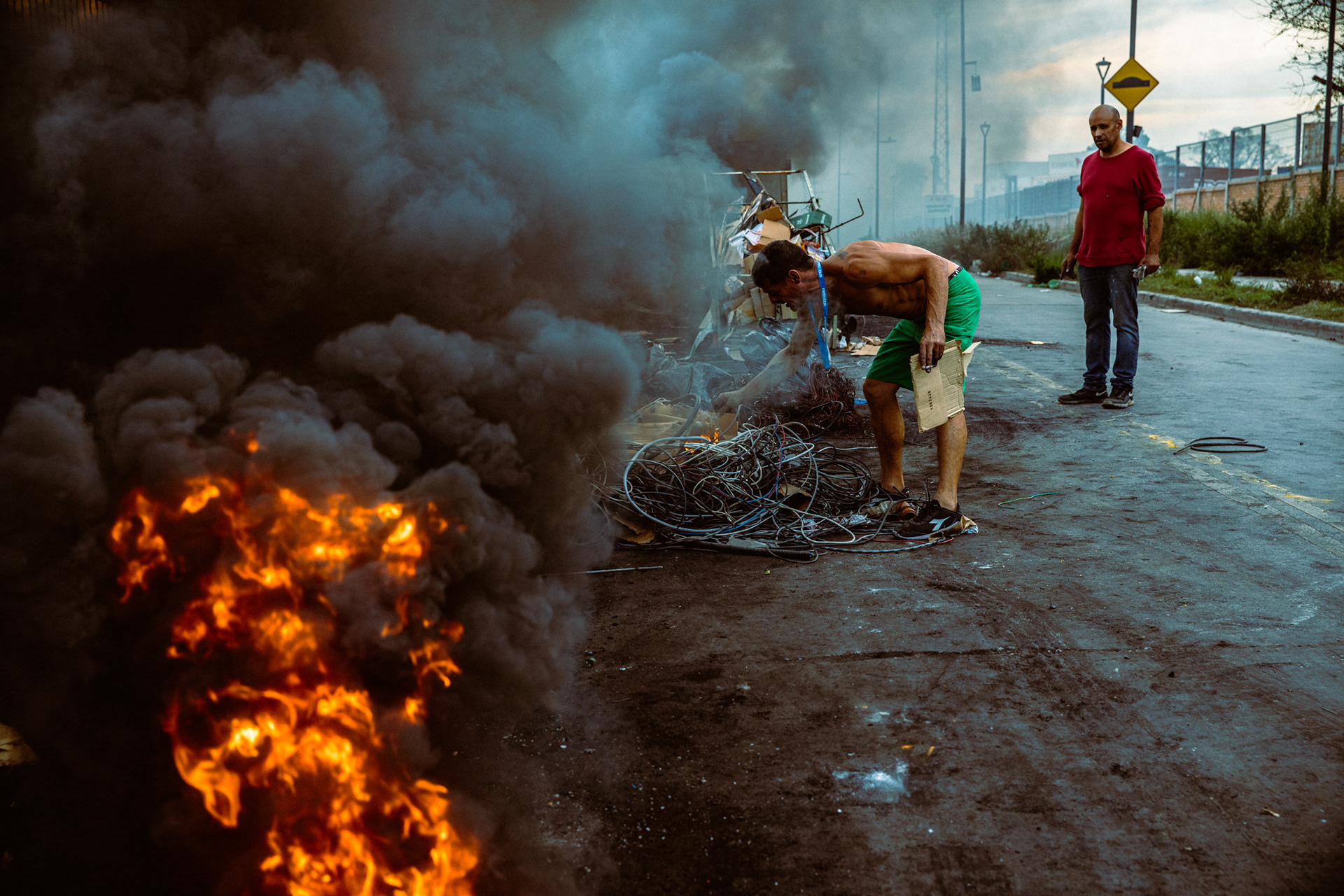 A man burning electrical cables with a huge fire while another man watches.