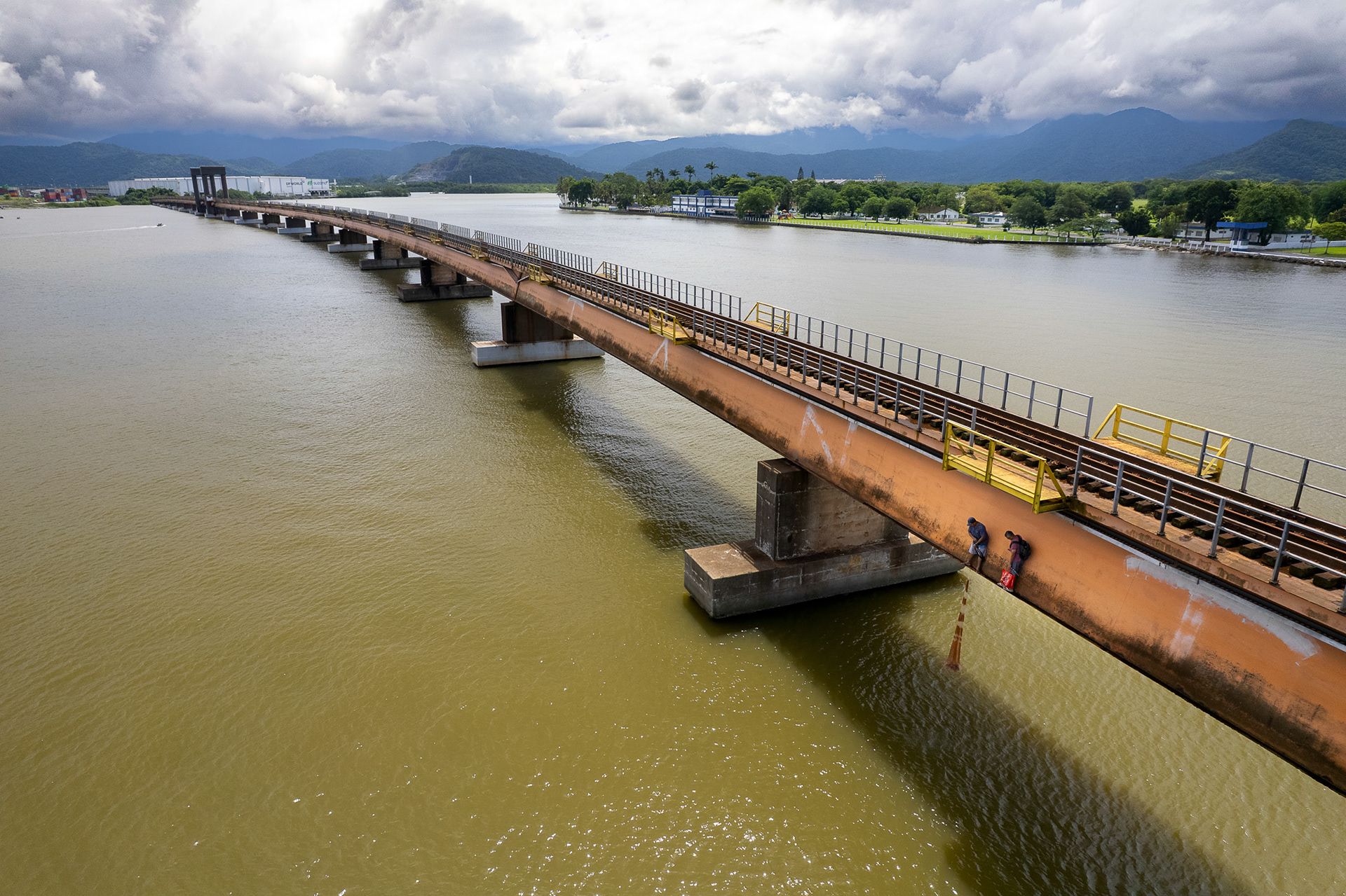 High above the estuary, fishermen walk along an old bridge in Santos, casting lines into muddy water as port development looms in the distance.