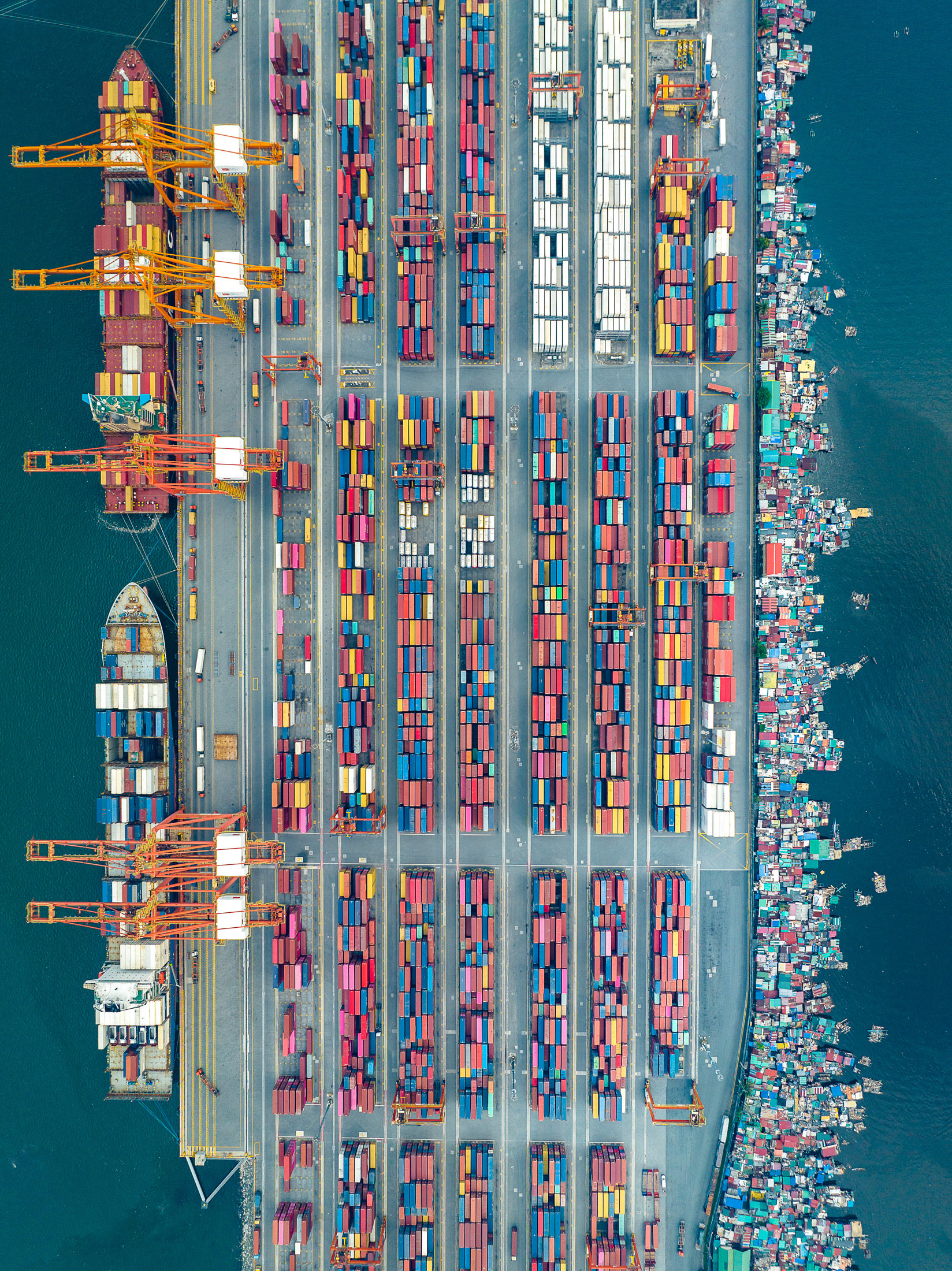 Aerial view of the Port of Manila, Philippines, showing neatly arranged shipping containers alongside floating informal settlements, highlighting inequality in urban logistics zones.