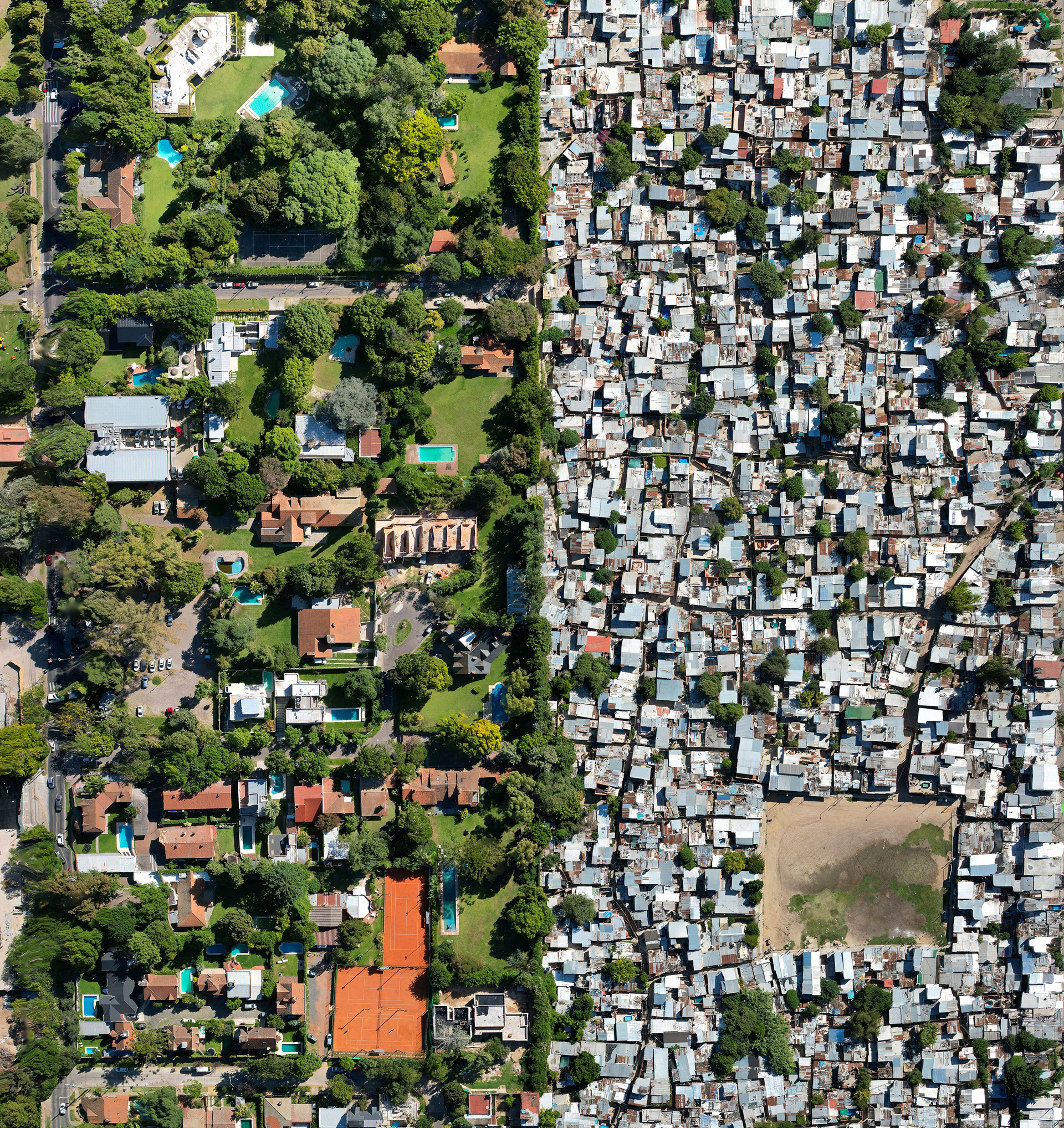 A drone photo of a slum next to a green neighborhood.