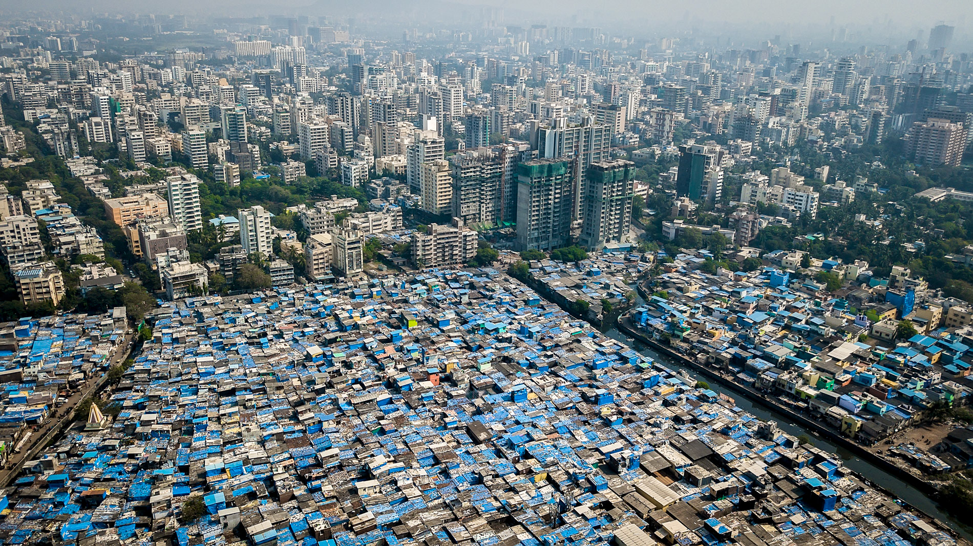 blue tarp slums exist right next to apartment buildings in mumbai india.
